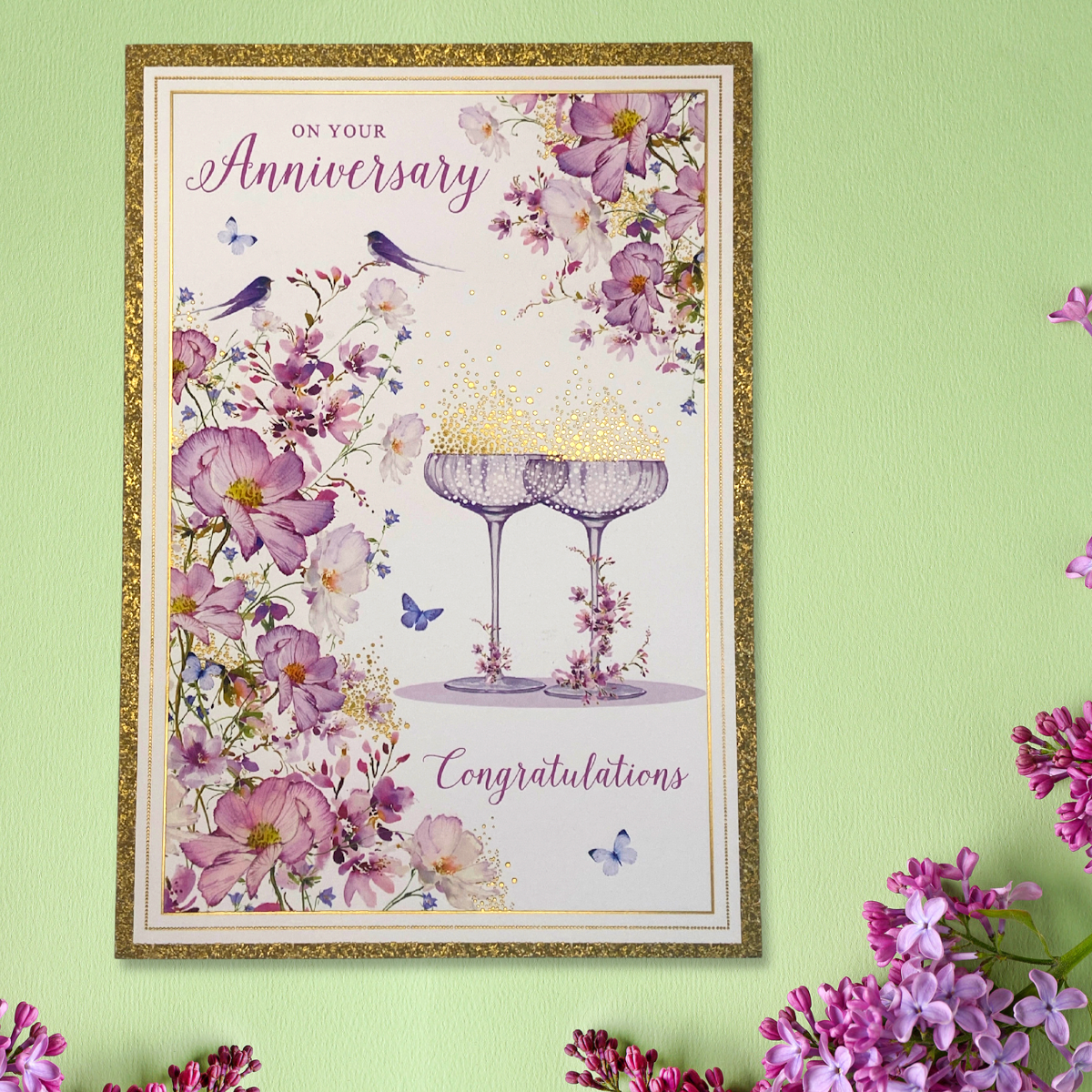 Front image showing to champagne glasses with floral borders and love birds. Gold glitter border