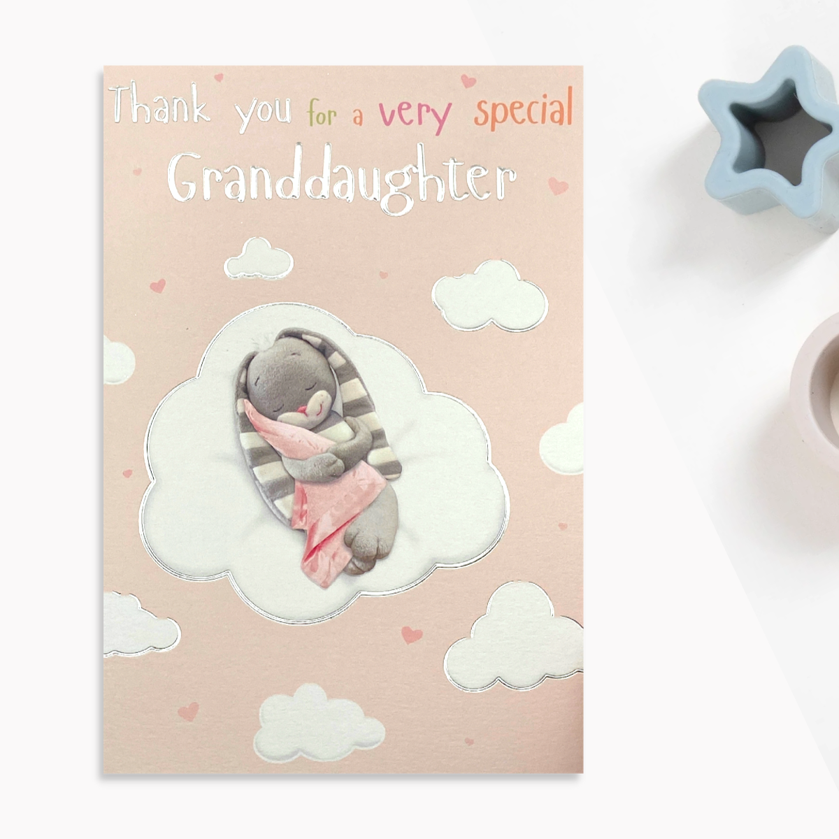 Front image with pink sky and white clouds surrounding bunny with blanket
