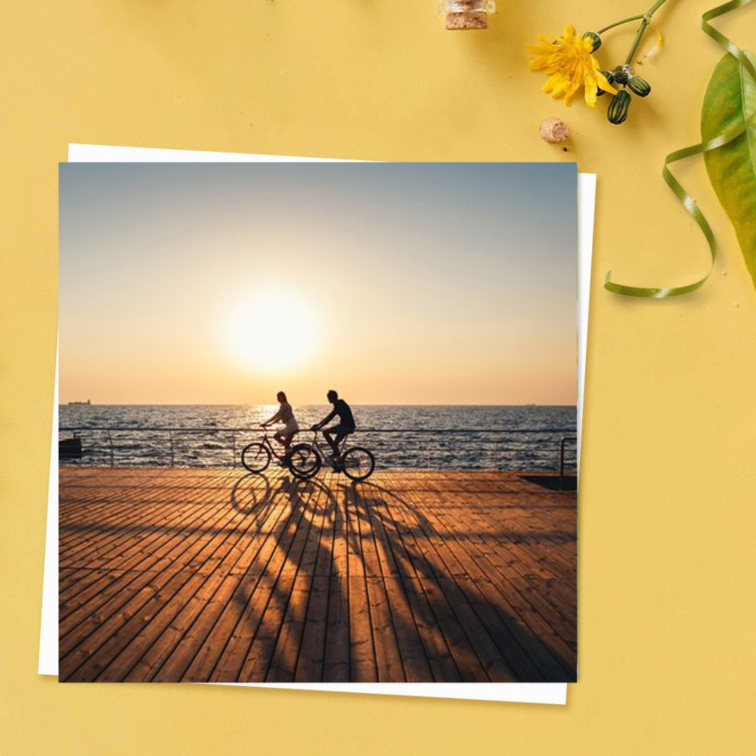 Two cyclists on promenade at sunset square card