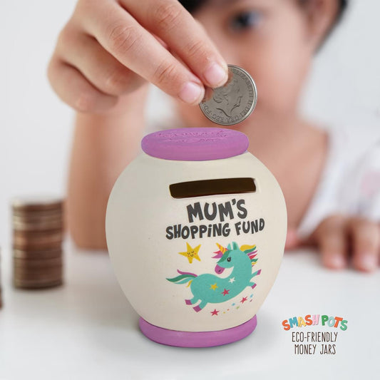 Mum's Shopping Fund single use Smash Pot for single use money saving. Smash the pot when full and bury pieces in the compost heap. Ivory pot with lilac lid and base and colourful unicorn image on the front. On reverse text reading - SAVE SMASH SPEND.