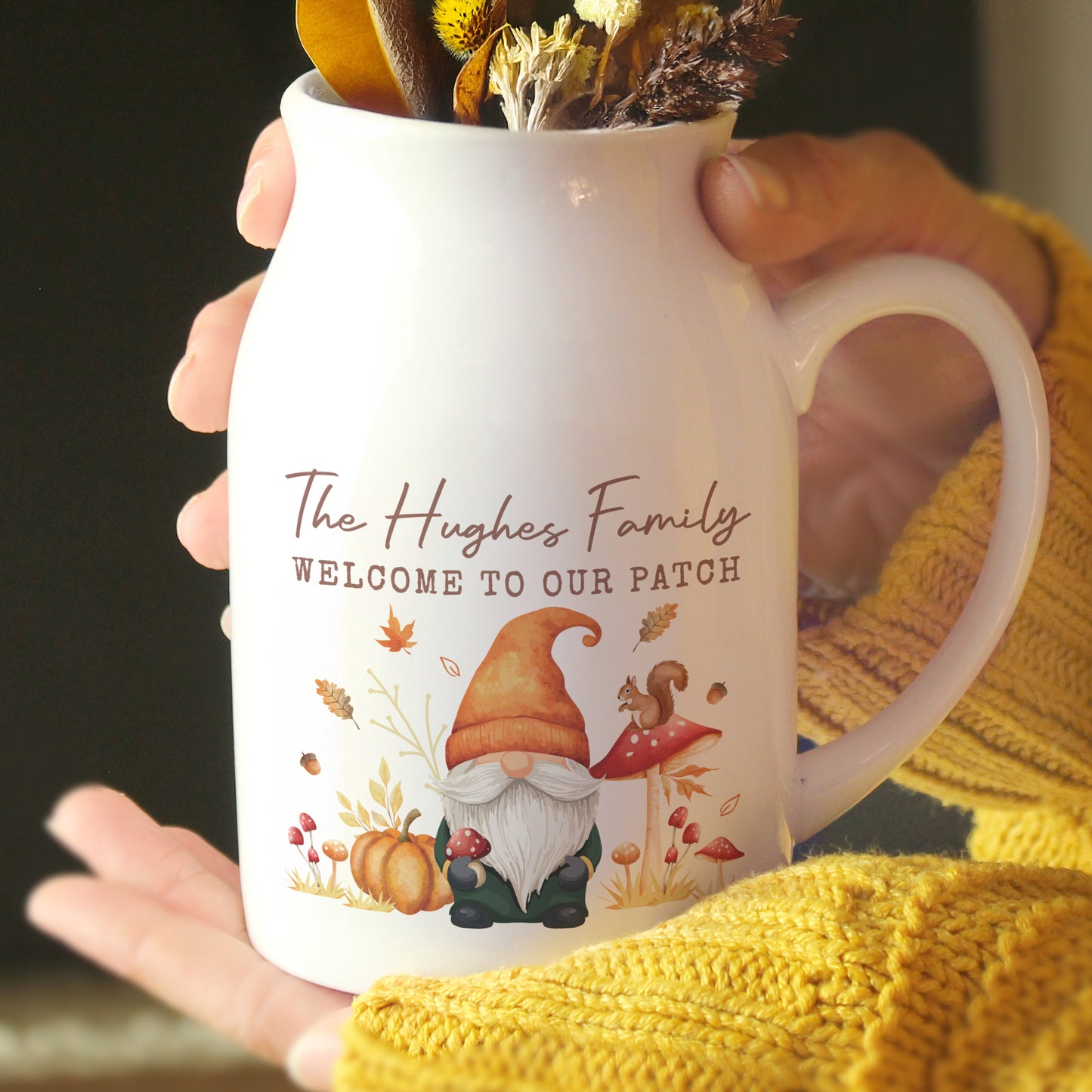 White mug with autumn-themed design and text held by a person wearing a yellow sweater.