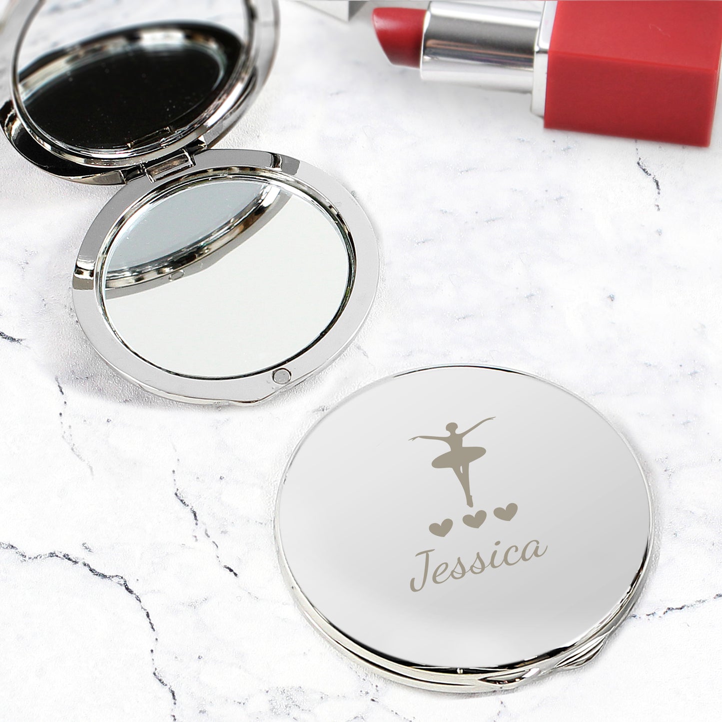 Compact mirror with engraved design and name on a marble surface with lipstick.