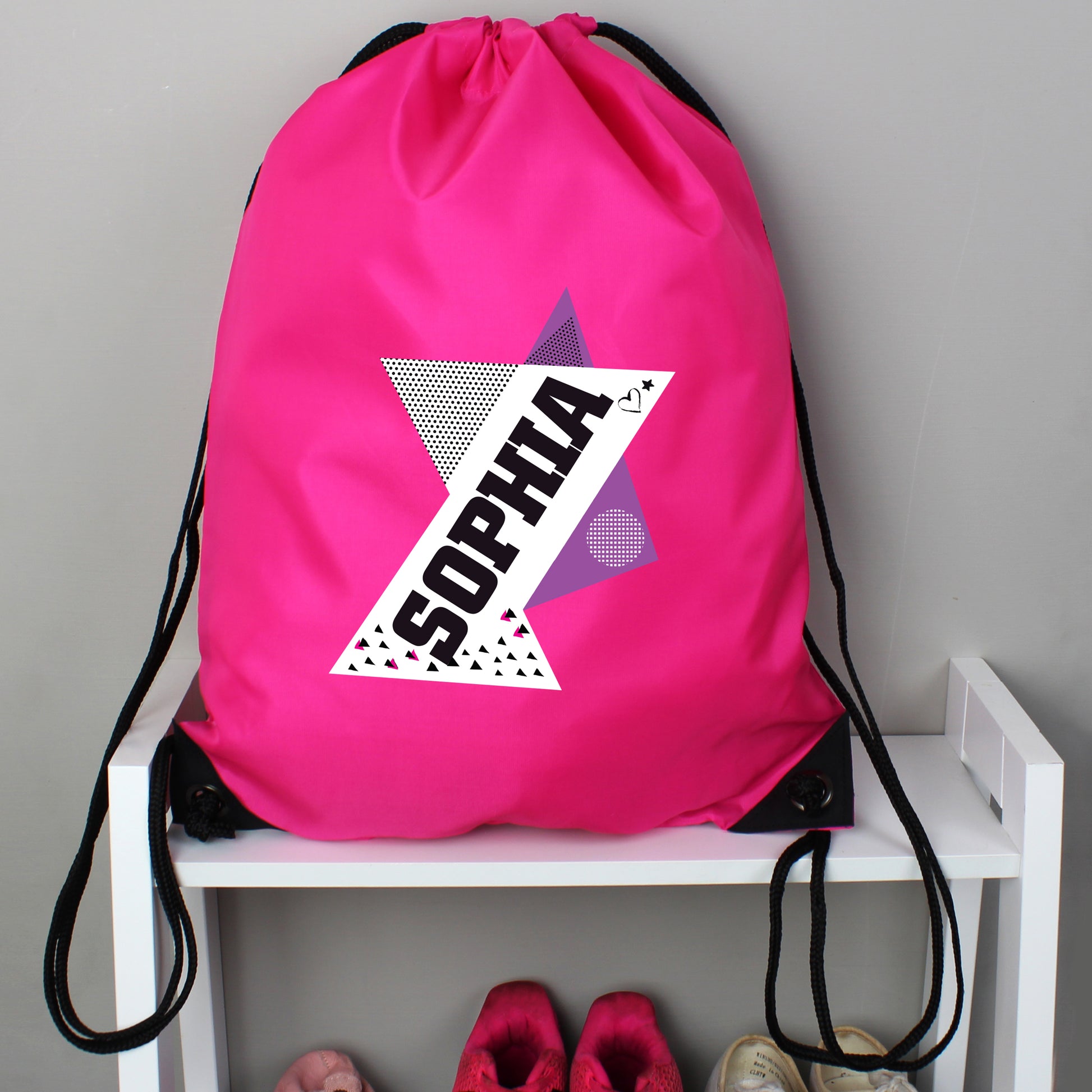 Pink drawstring bag with 'SOPHIA' design on a white shelf against a gray wall.