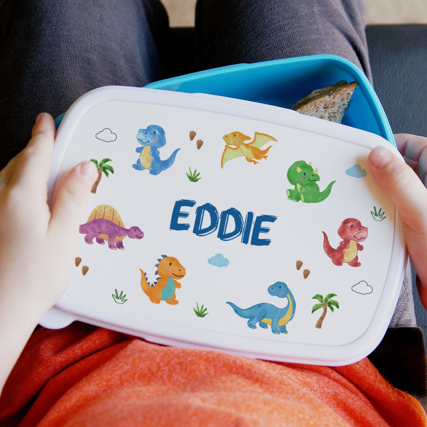 Children's lunchbox with dinosaur illustrations and the name 'Eddie' on a white background.
