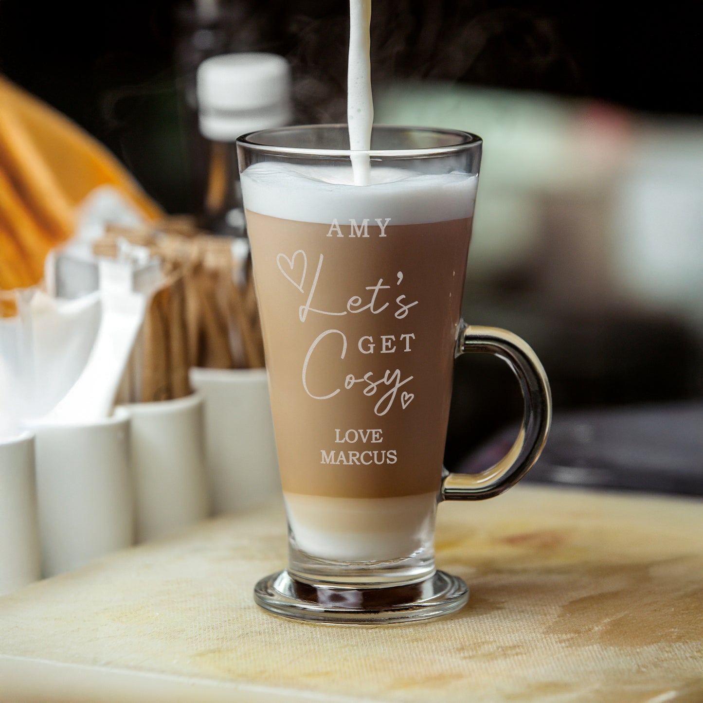 Glass mug with personalized text being filled with a creamy liquid, likely coffee.