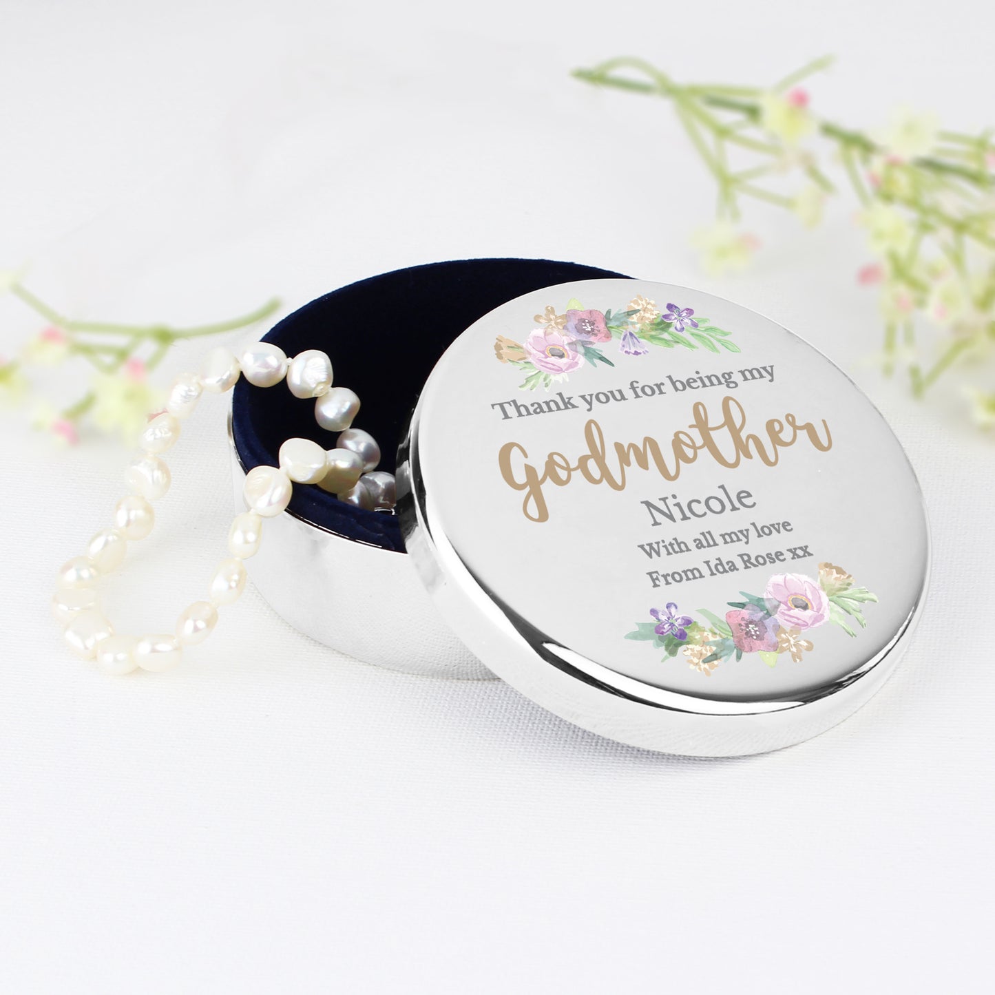 Round silver container with floral design and pearl necklace on a white background
