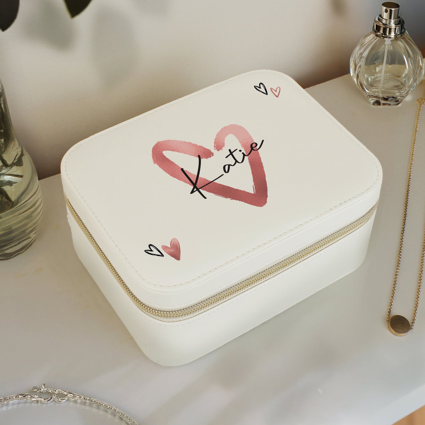 White jewelry box with 'Katie' and heart designs on a surface with a necklace and perfume bottle.