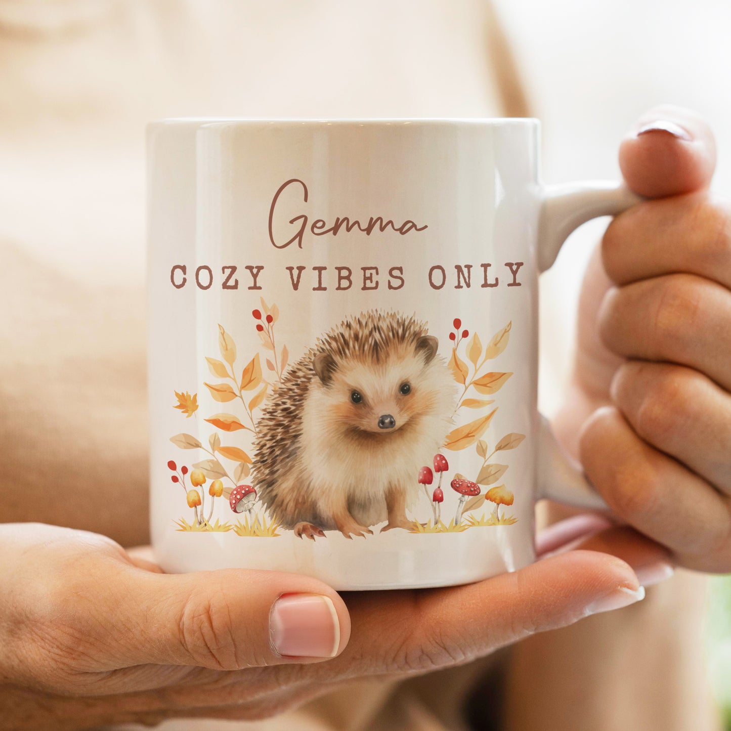 Person holding a mug with a hedgehog design and text 'Gemma COZY VIBES ONLY'.