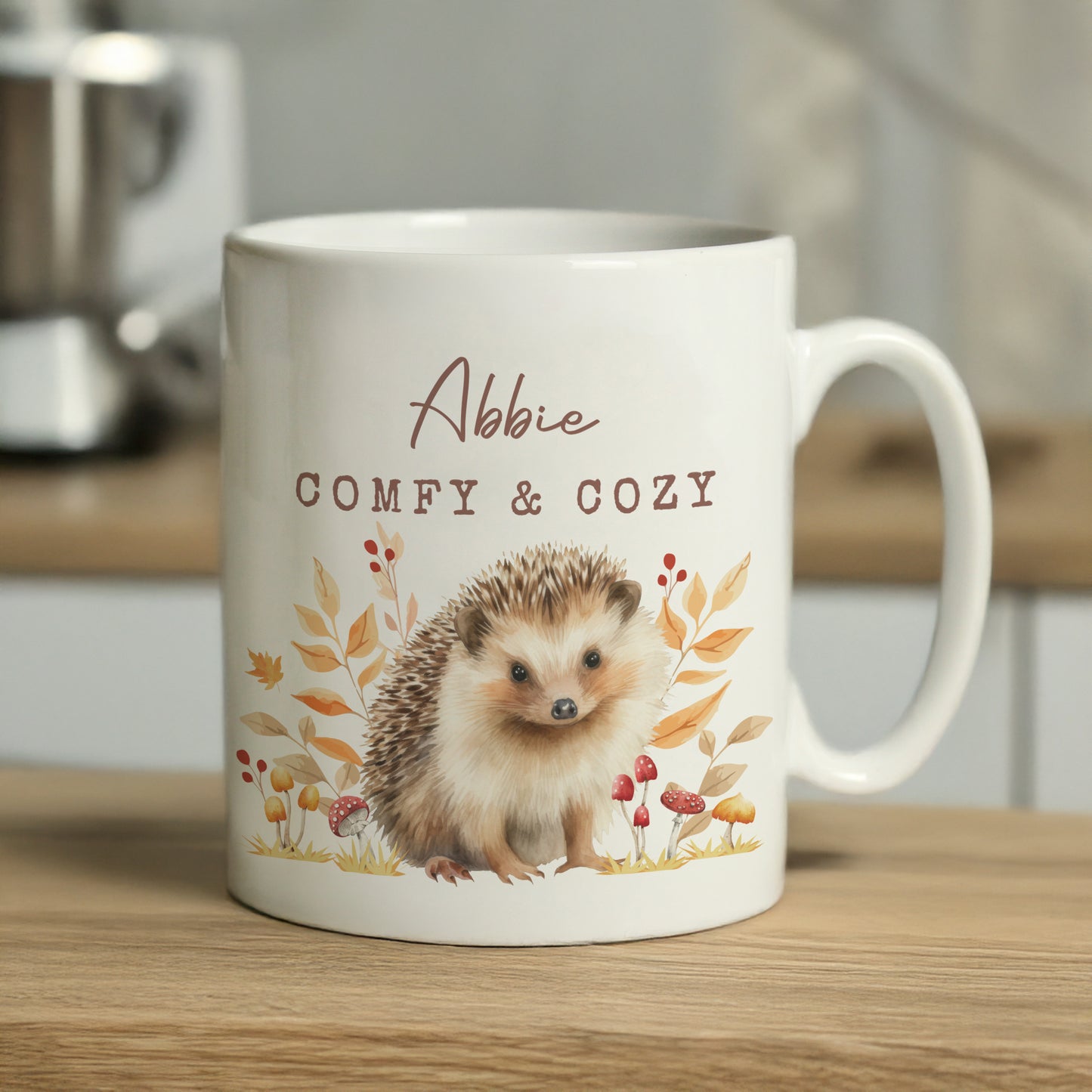 Mug with hedgehog design and text 'Abbie Comfy & Cozy' on a wooden surface.