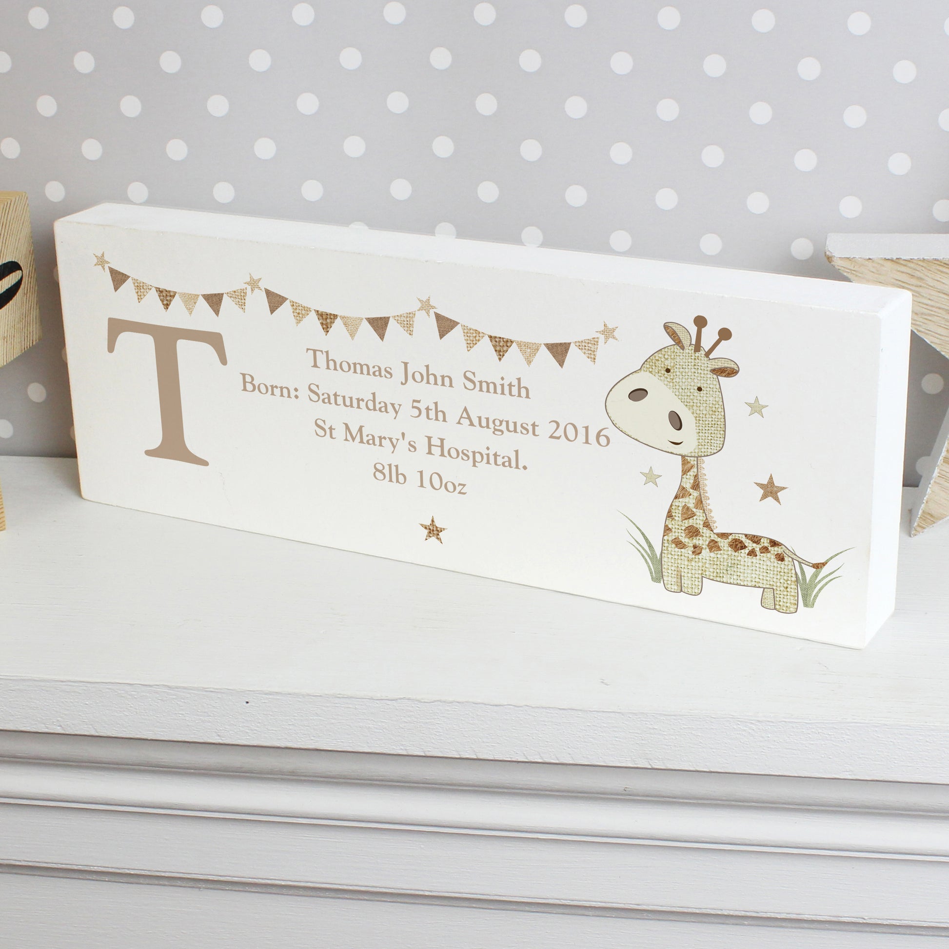 Personalised baby block with giraffe illustration and text on a white surface with polka dot background