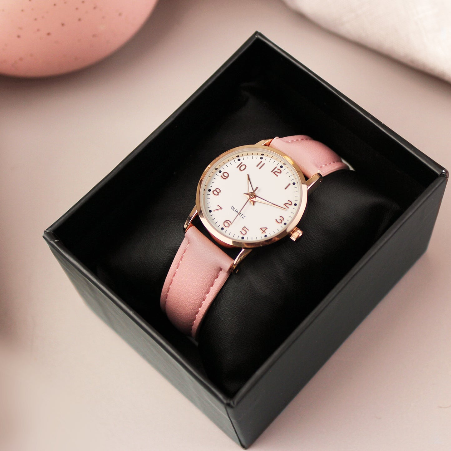 Watch with pink strap and rose gold case in a black box on a beige background