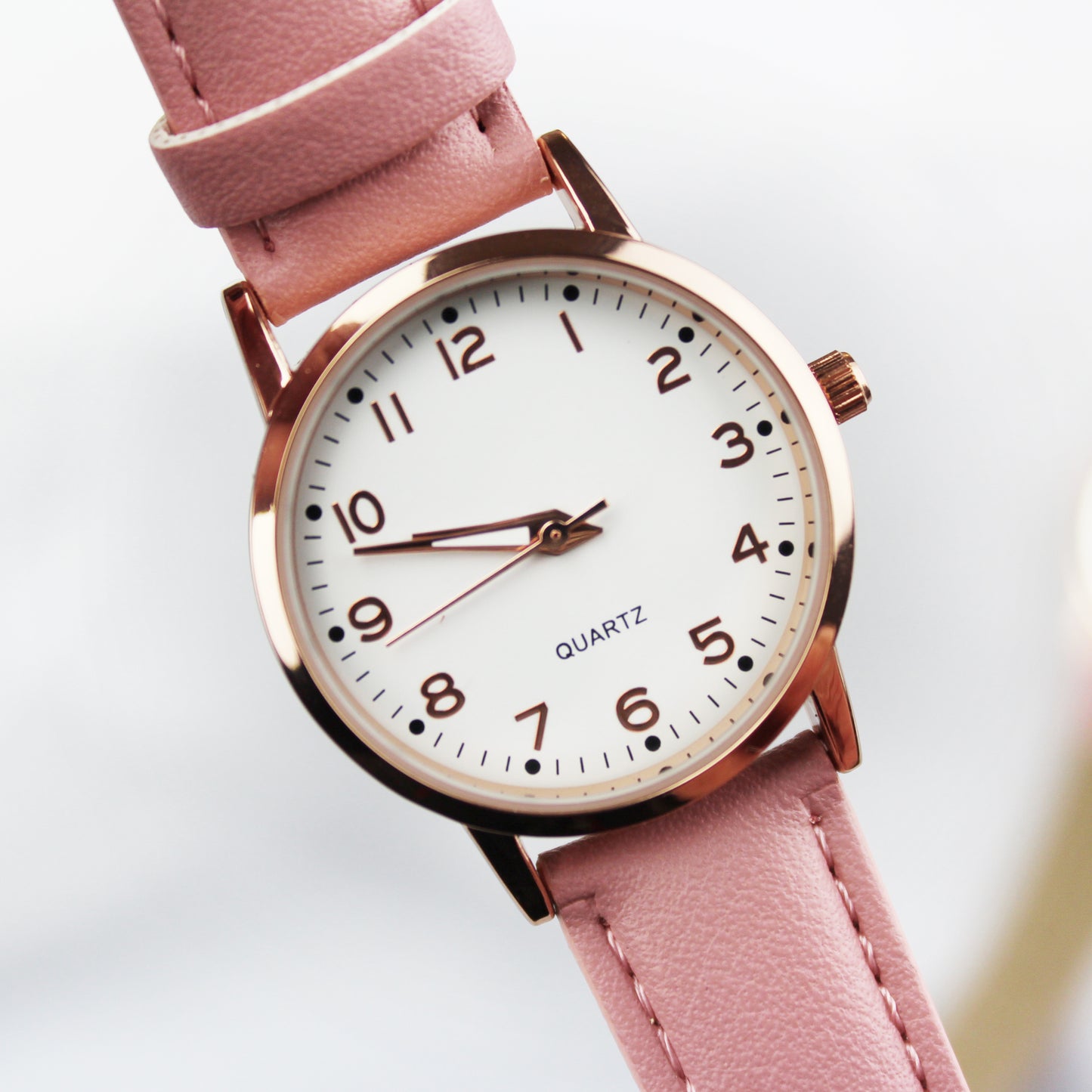 Watch with pink strap and rose gold casing on a white background