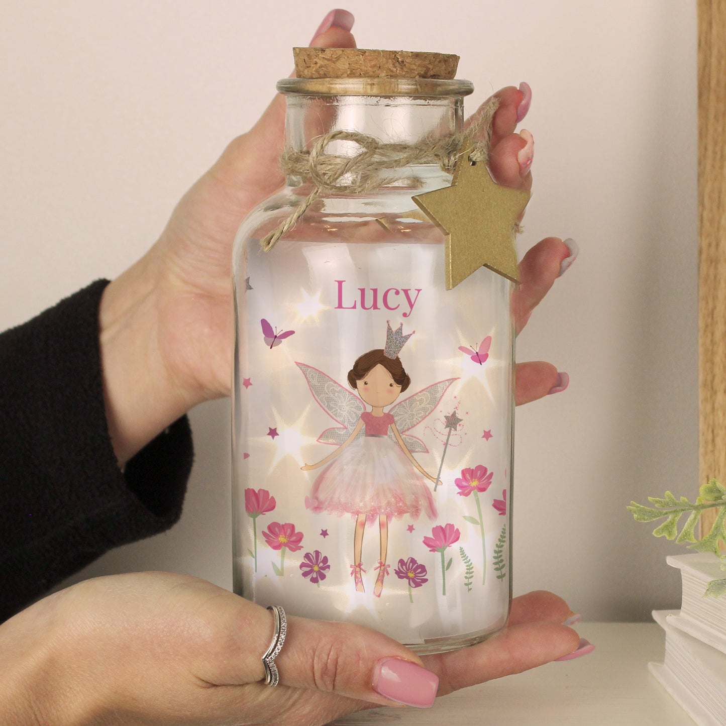 Glass jar with fairy design and 'Lucy' text, held by a person.