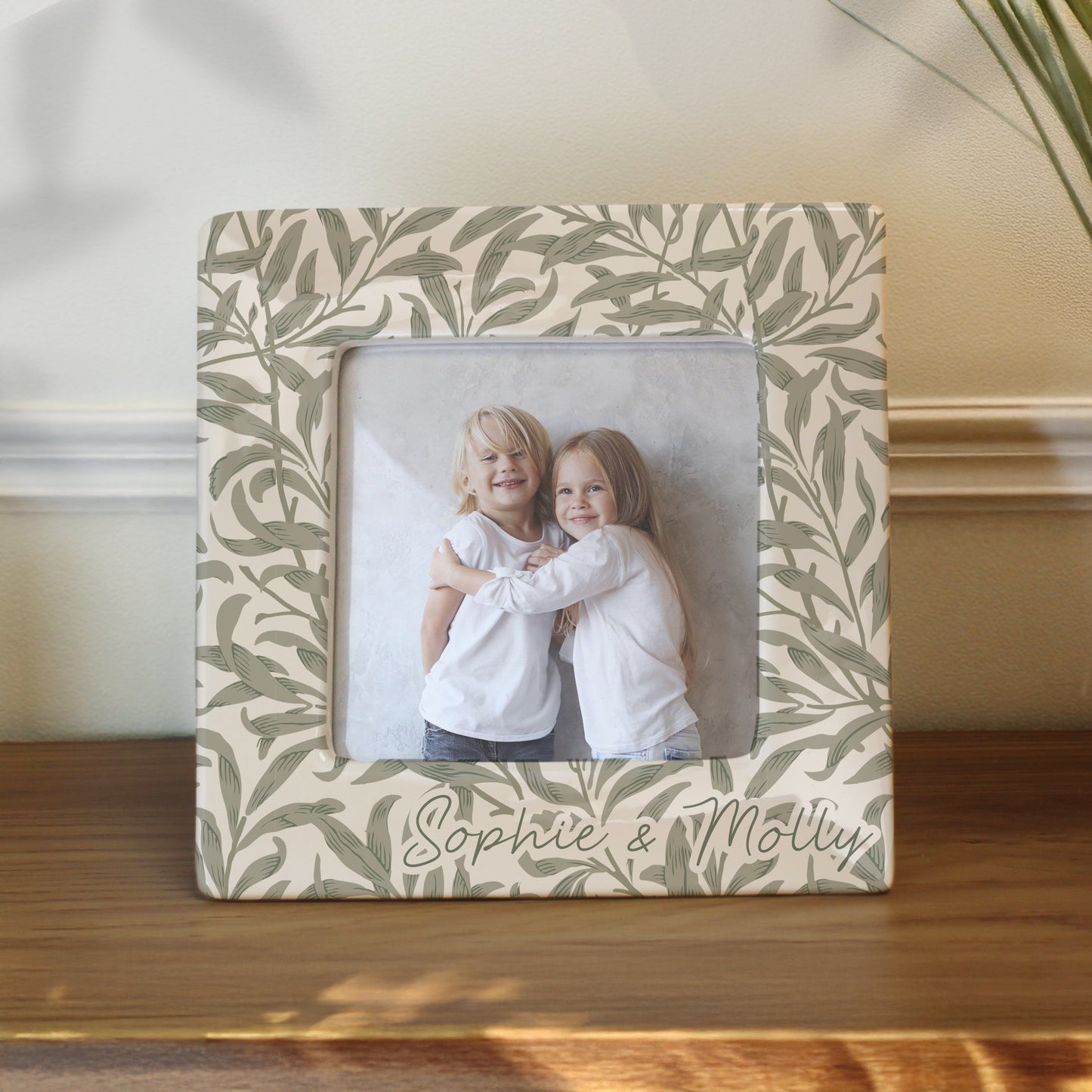 Decorative photo frame with leaf pattern and two children's photo inside, placed on a wooden surface.