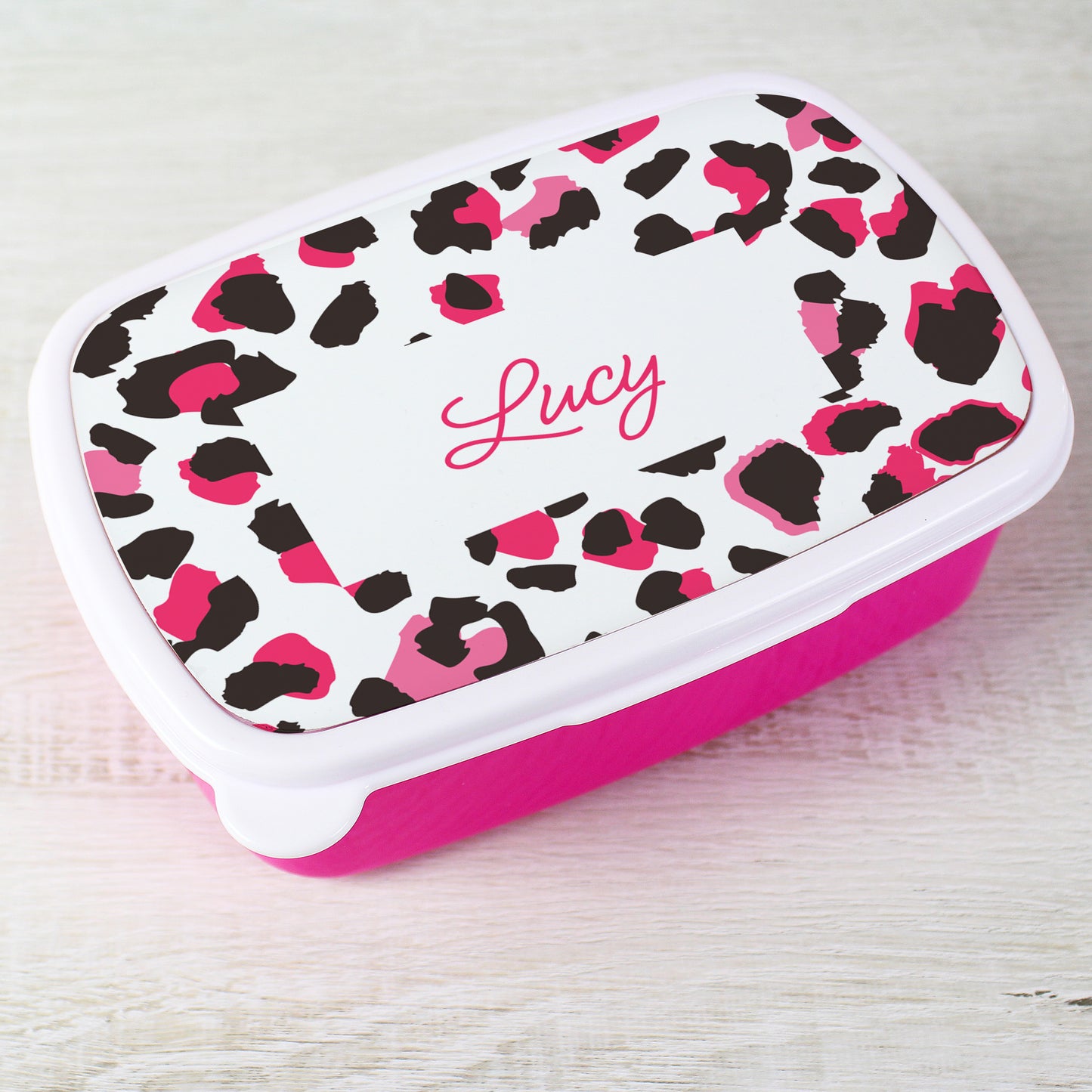 Pink and black leopard print container with 'Lucy' on a light wooden surface