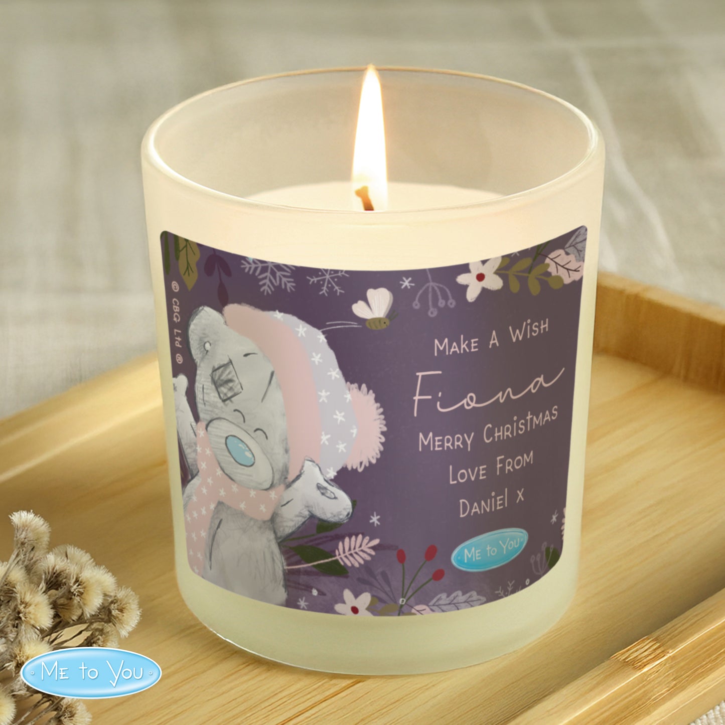 Candle with a decorative label featuring a cartoon character on a wooden surface.