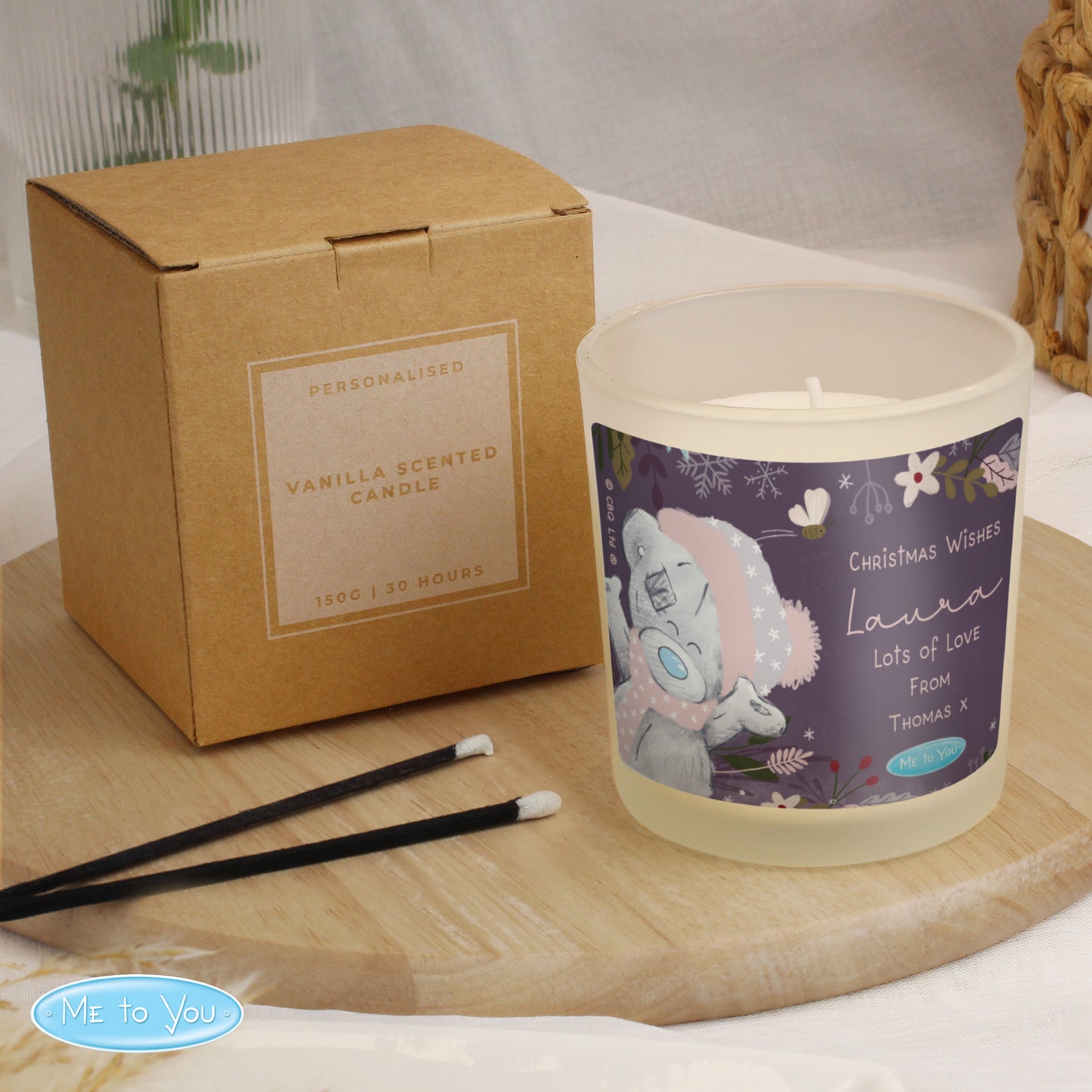 Personalised candle with a decorative label next to its packaging on a wooden surface.