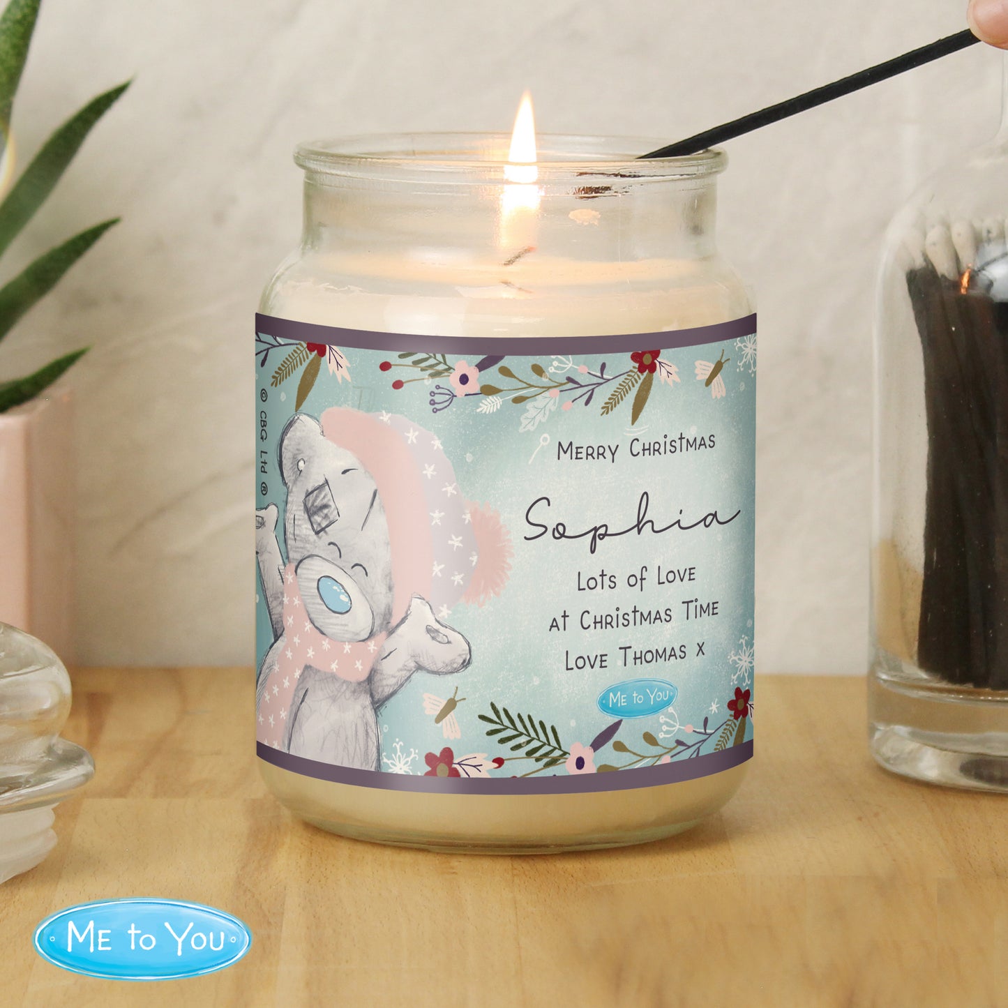 Candle in a jar with a label featuring a bear design and text, on a wooden surface.