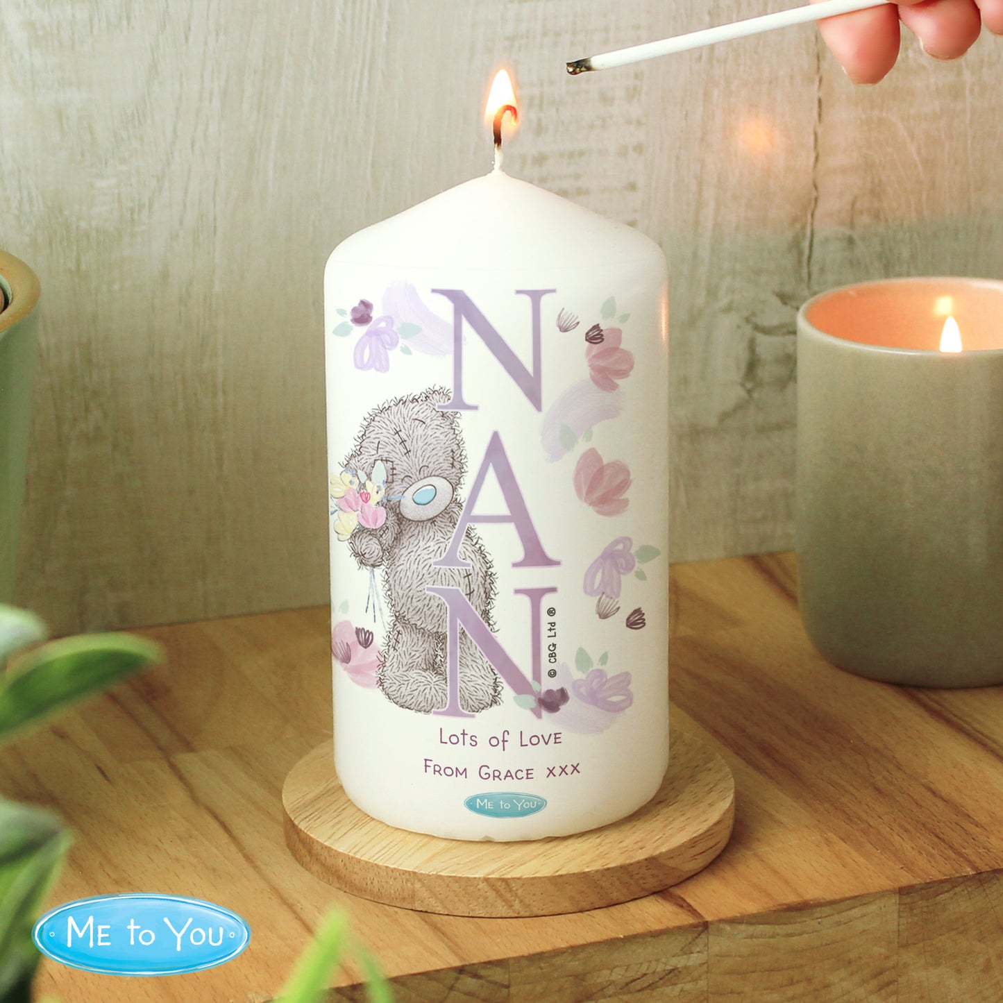 Candle with 'NAN' and a teddy bear design, being lit on a wooden surface.