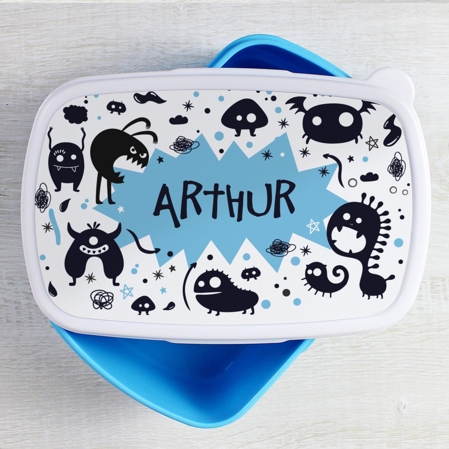 Lunch box with black and white monster design and blue accents on a light grey background