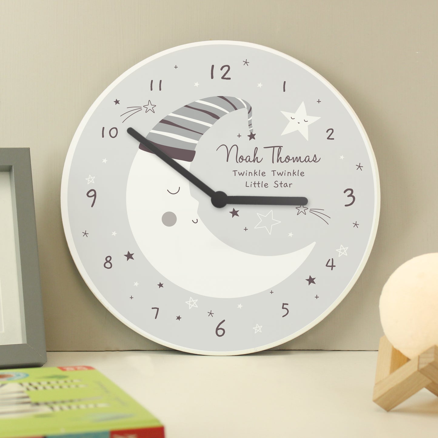 Children's wall clock with moon and star design on a beige wall.
