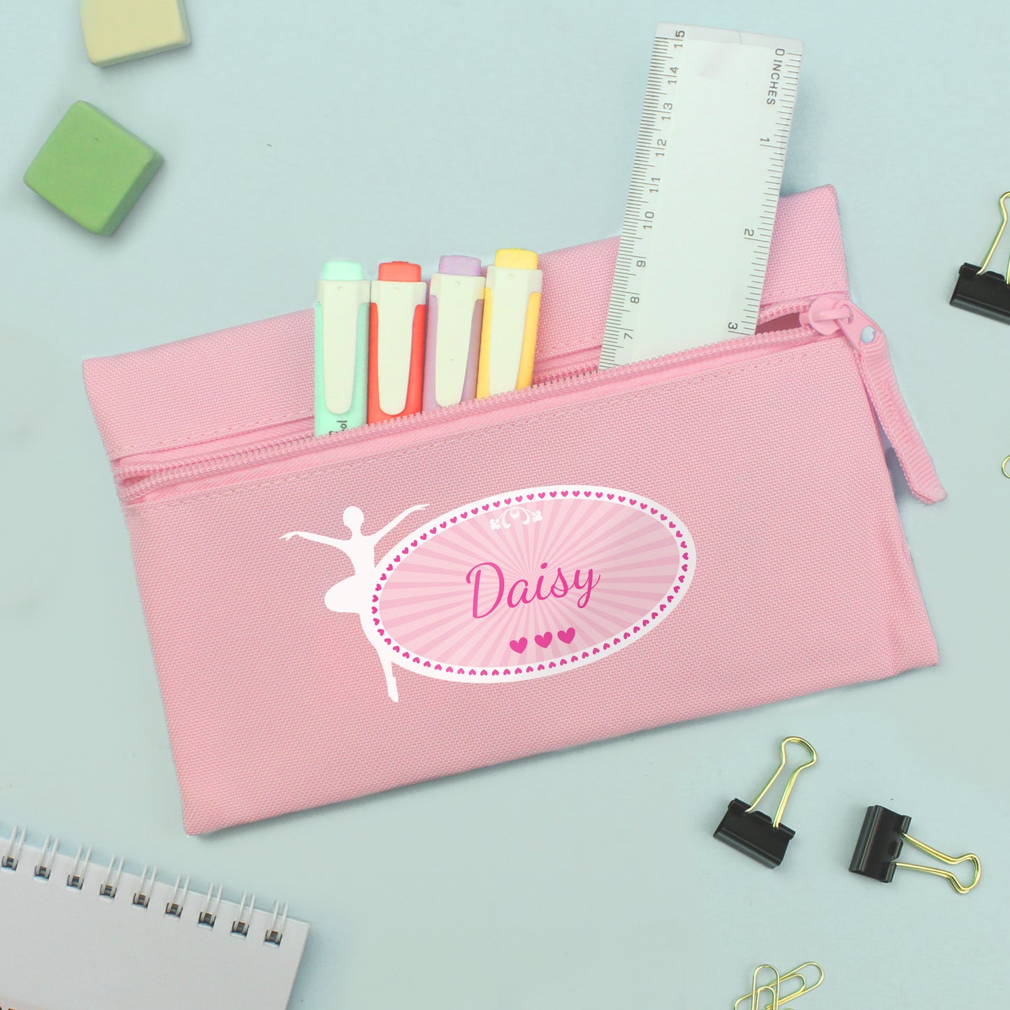 Pink pencil case with 'Daisy' design, filled with stationery items on a light blue background.