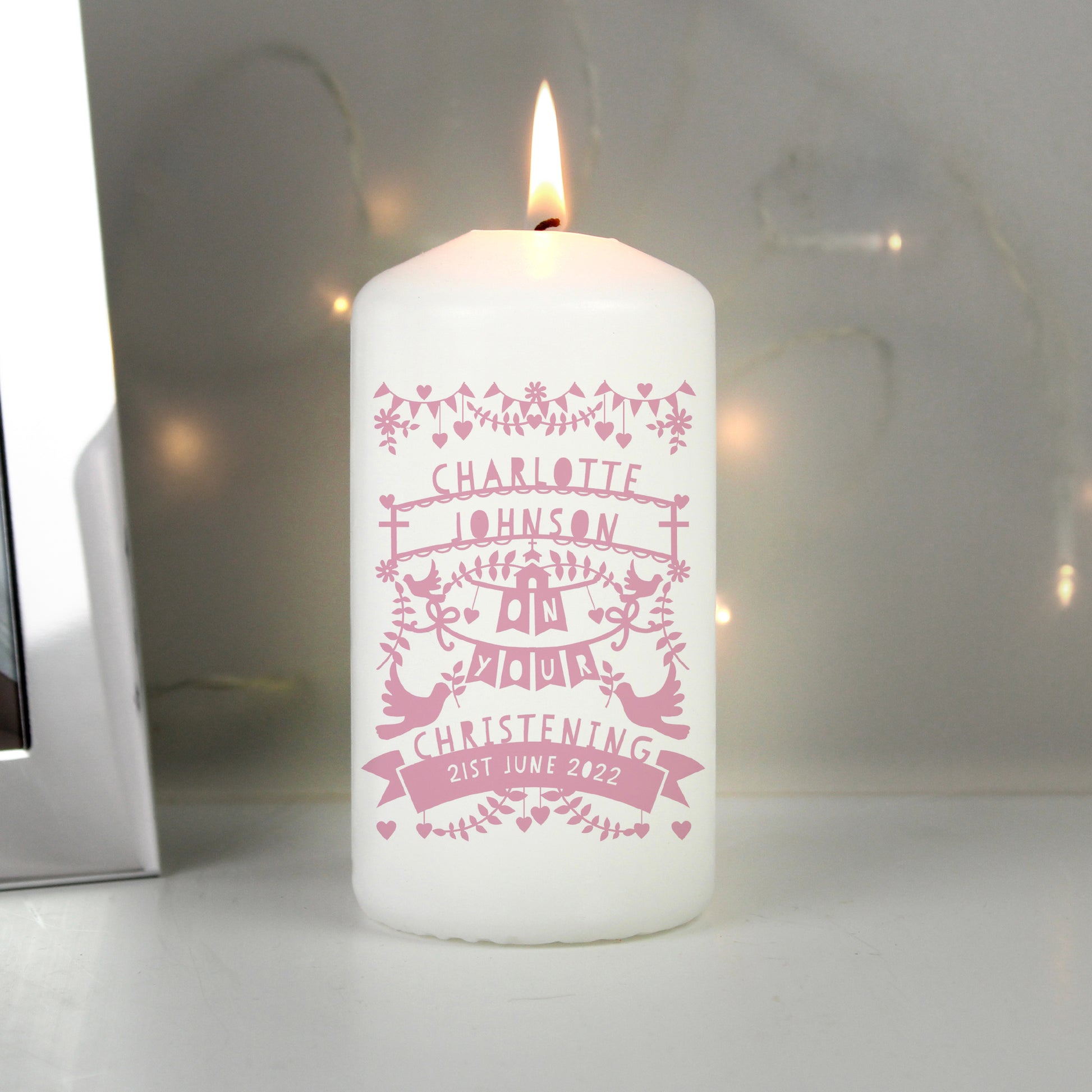 White candle with pink personalised design on a white surface