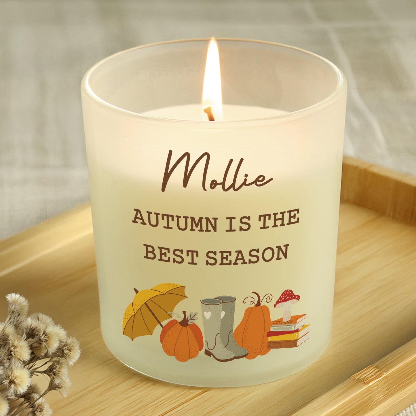 Candle with 'Autumn is the Best Season' text and autumn-themed illustrations on a wooden surface.