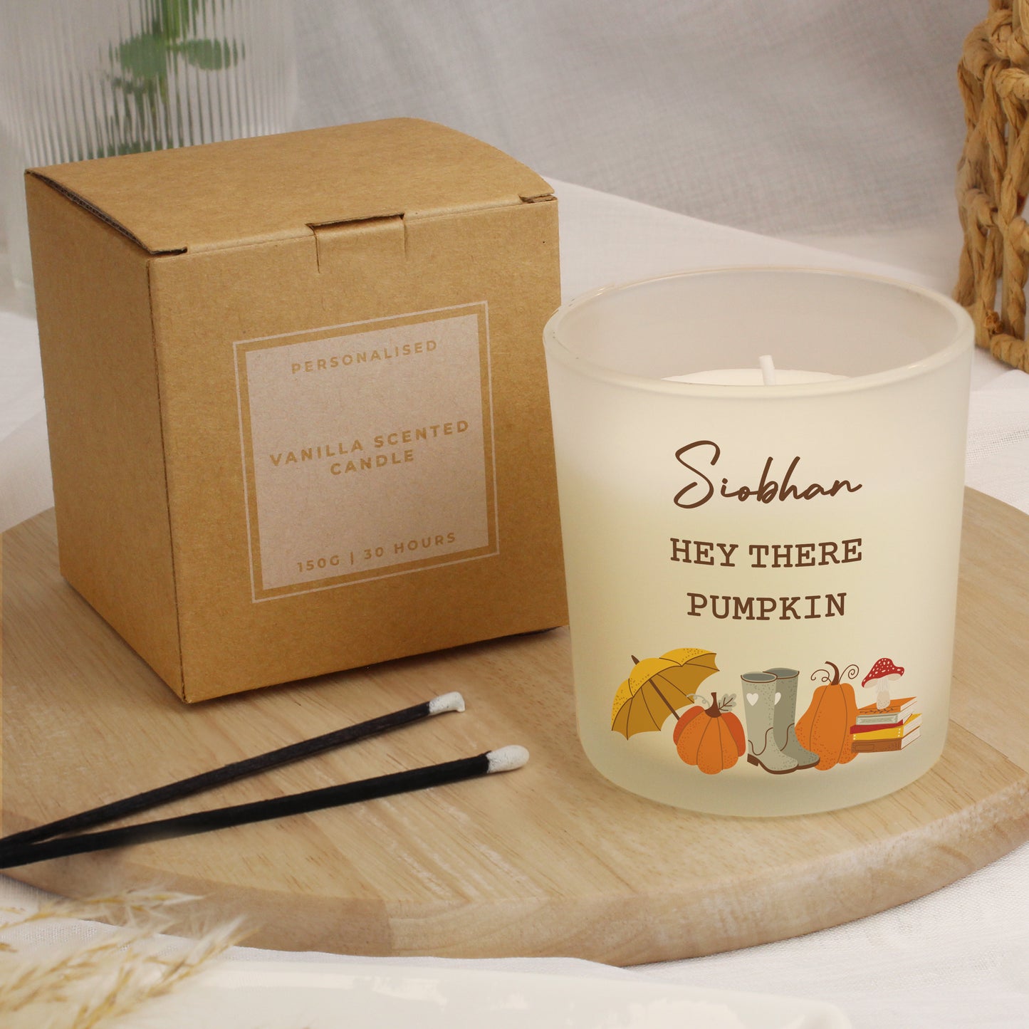 Vanilla scented personalised pumpkin frosted candle with 'Hey There Pumpkin' text and illustrations next to its packaging on a wooden surface.