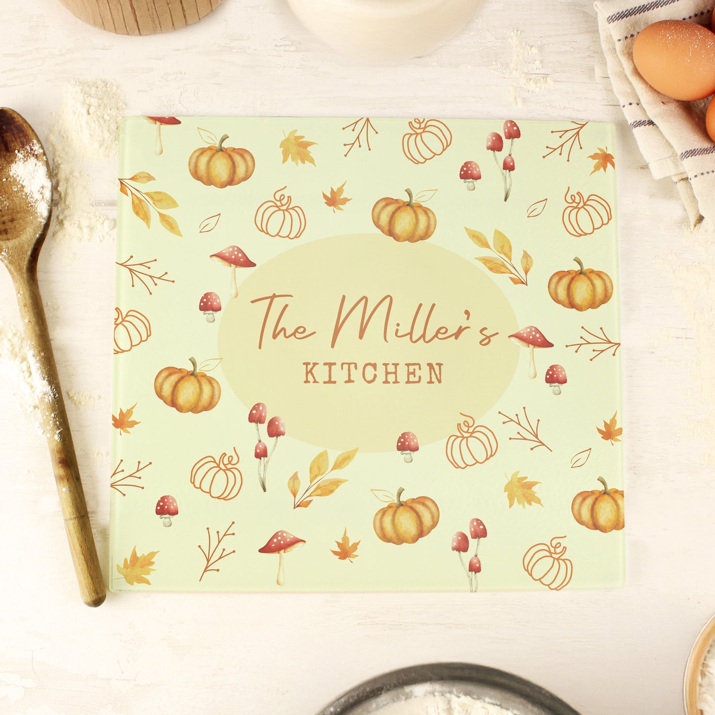 Personalised glass chopping board with autumn pumpkin design and 'The Miller's Kitchen' text on a table.