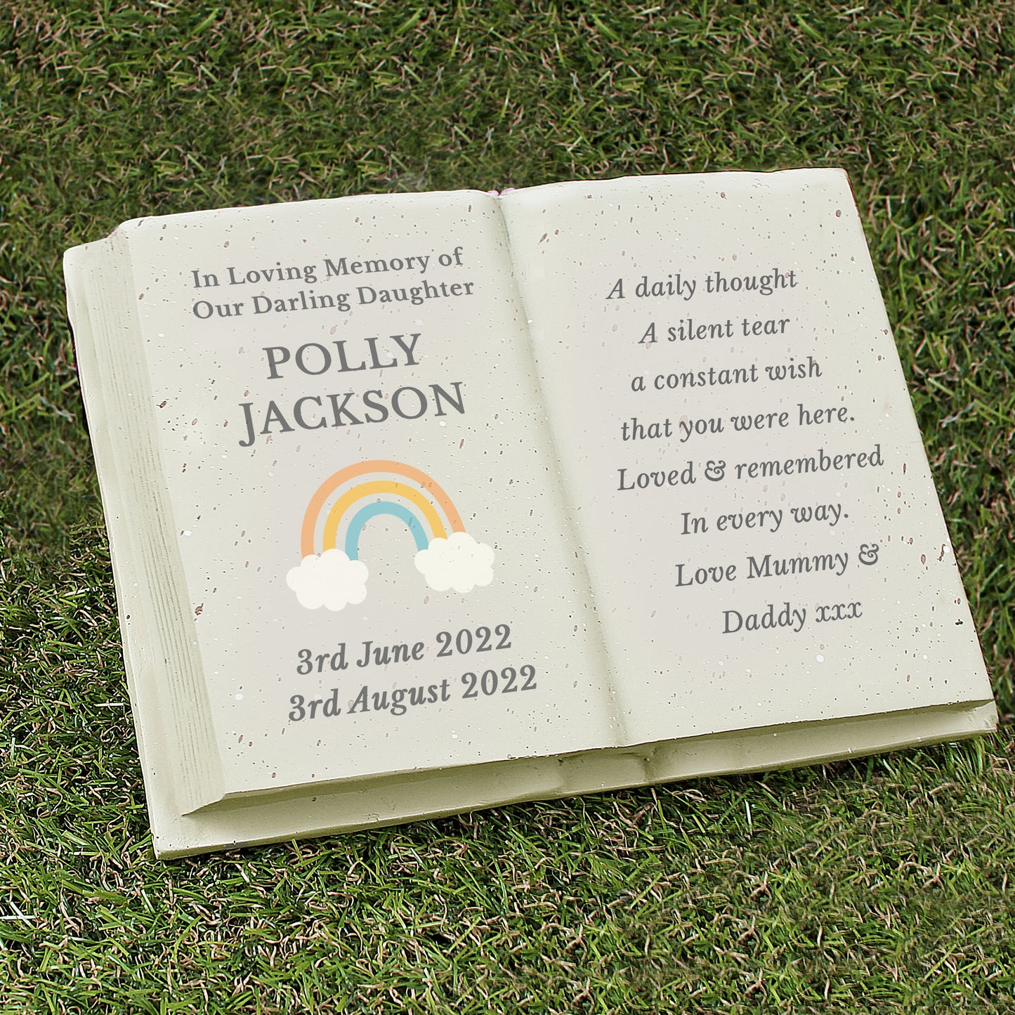 Memorial book with engraved text and rainbow design on grass