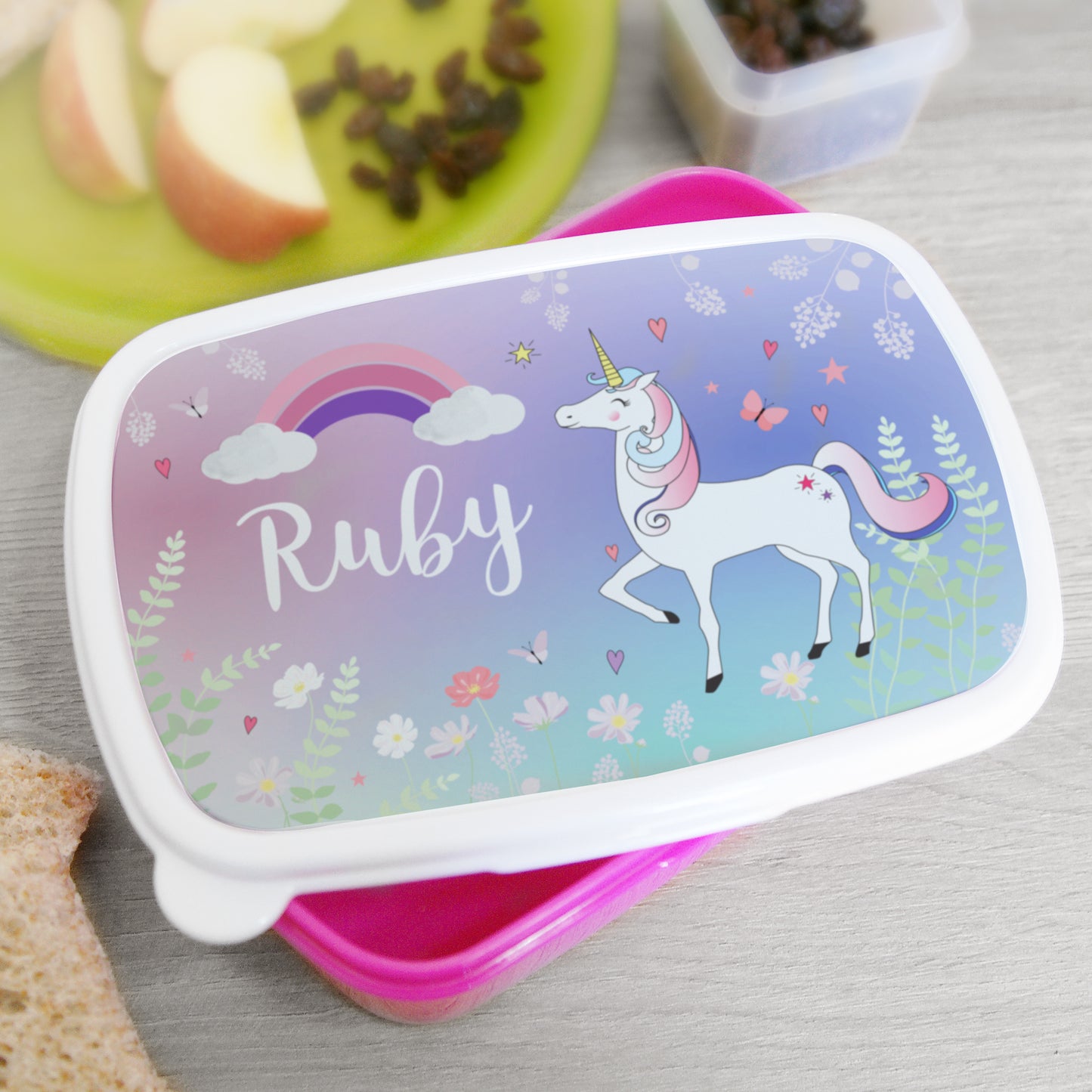 Lunch box with unicorn design and 'Ruby' on a table with snacks