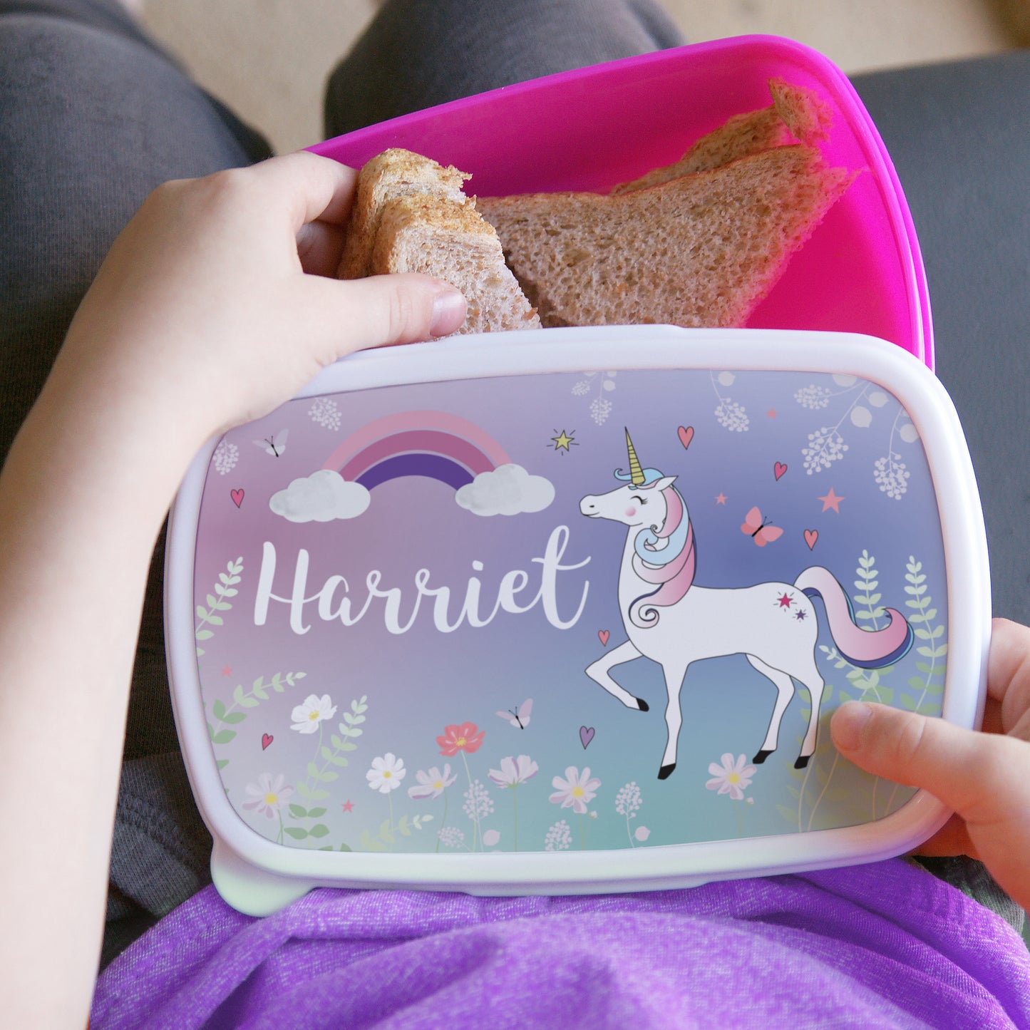 Lunchbox with unicorn design and 'Harriet' on it, held by a child.
