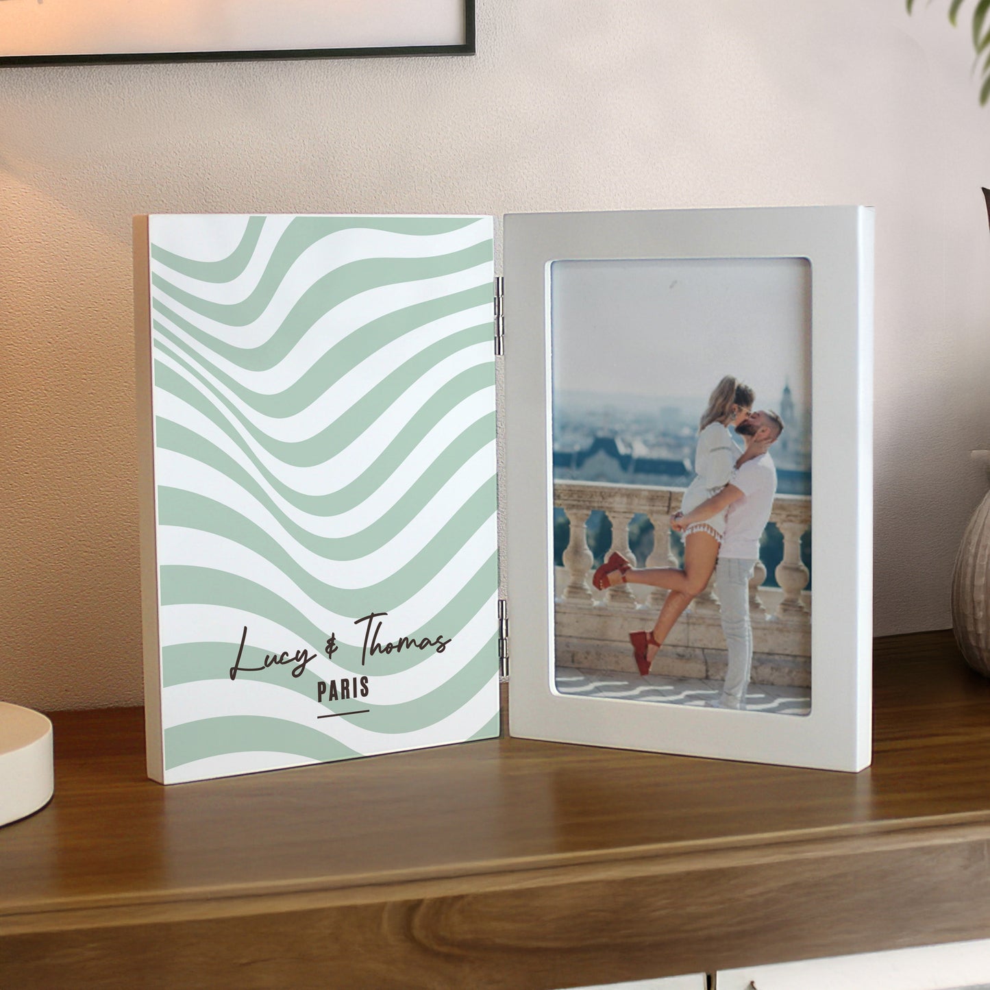 Open photo album with wavy design on one side and couple on a balcony on the other, on a wooden surface.
