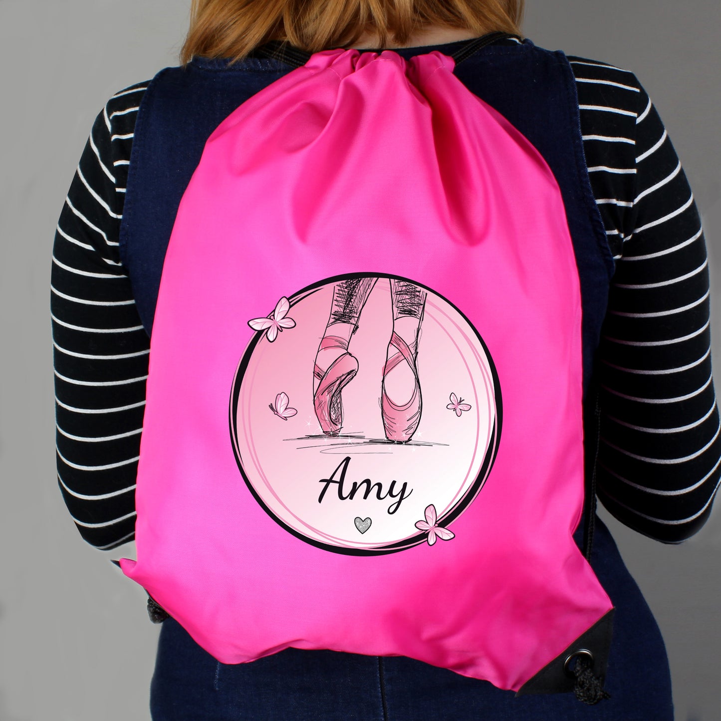 Person wearing a pink drawstring bag with ballet design and name 'Amy'.