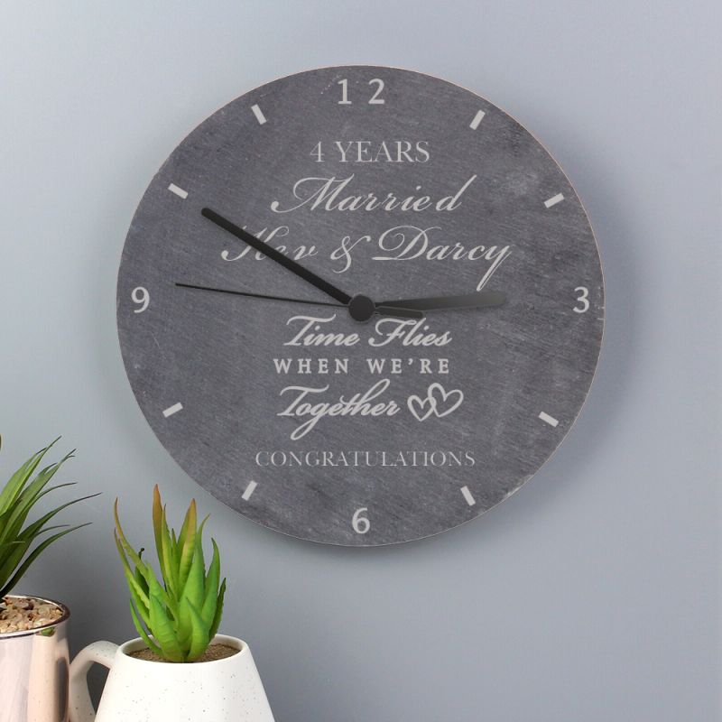 Wall clock with personalised message on a grey wall with plants below.