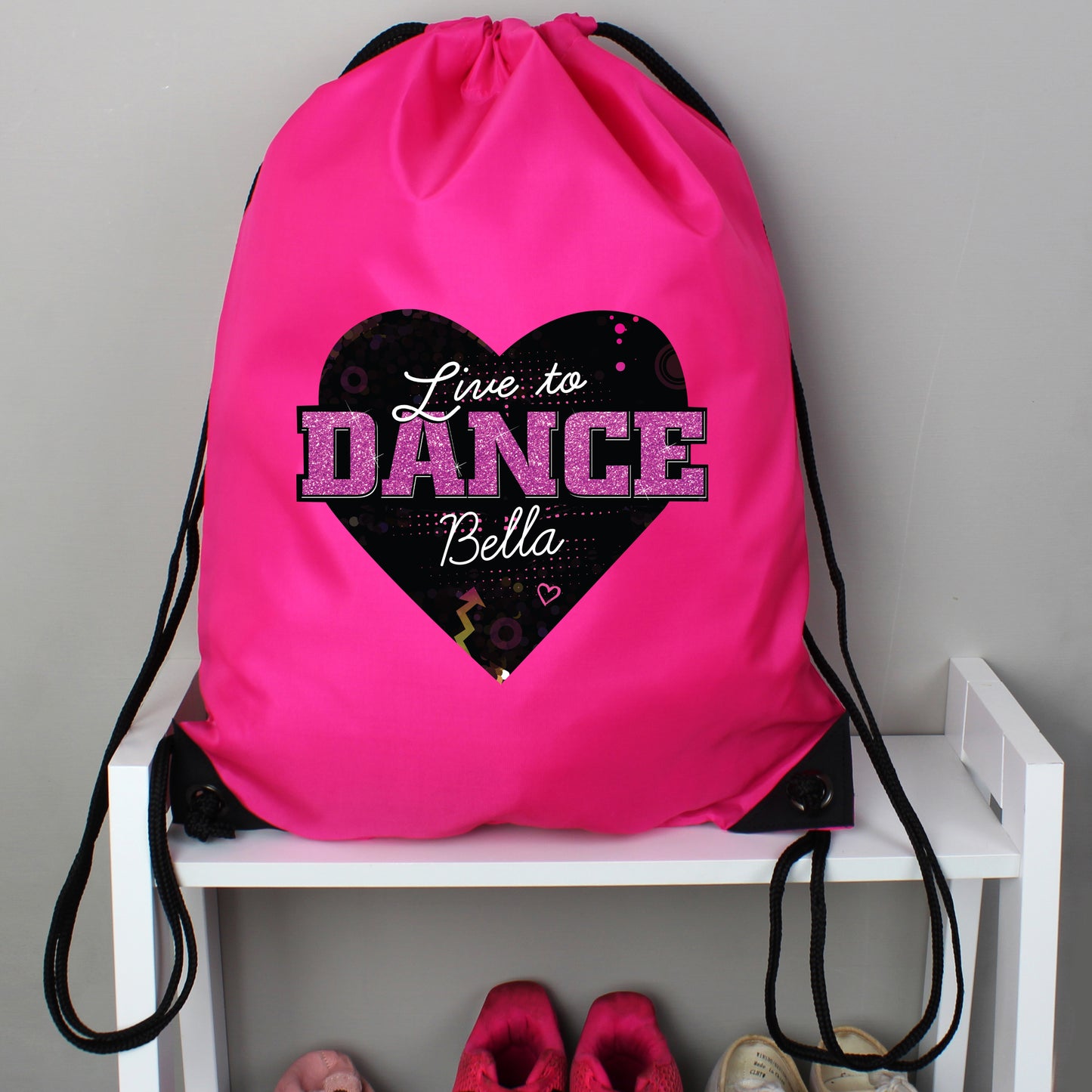 Pink drawstring bag with 'Live to Dance Bella' design on a white shelf.