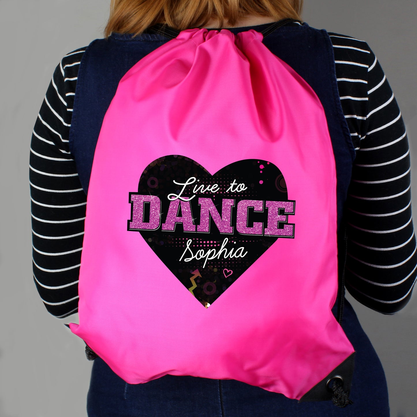 Pink drawstring bag with 'Live to Dance Sophia' design on a person wearing a striped shirt.