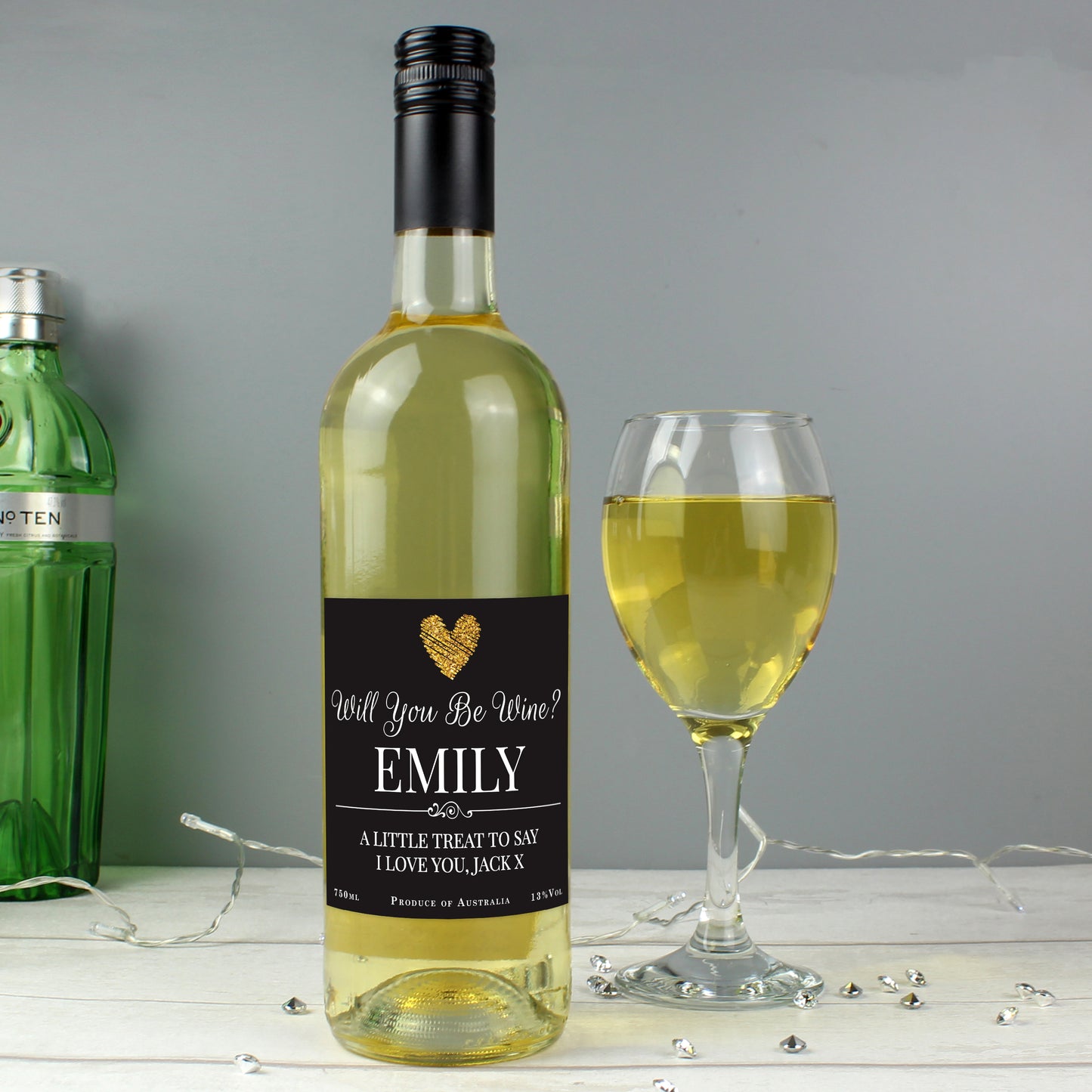 Bottle of white wine with a personalised label next to a glass of wine on a grey background