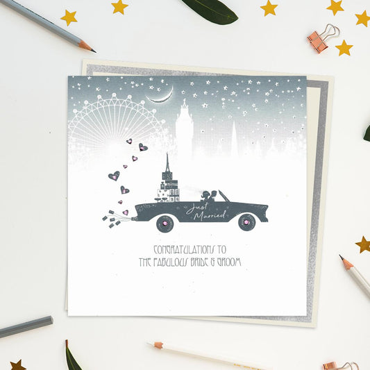 Stunning, Luxury, Handcrafted Wedding Day Design From Five Dollar Shake. Image Shows A Black Car In Silhouette Full Of Gifts With A Skyline In The Background. On The Side Of The Car Is Written-Just Married. Caption: Congratulations To The Fabulous Bride And Groom. With Jewel Embellishments And Biodegradable Glitter Accents. Blank Inside For Own Message. Warm White Envelope With Silver Border.