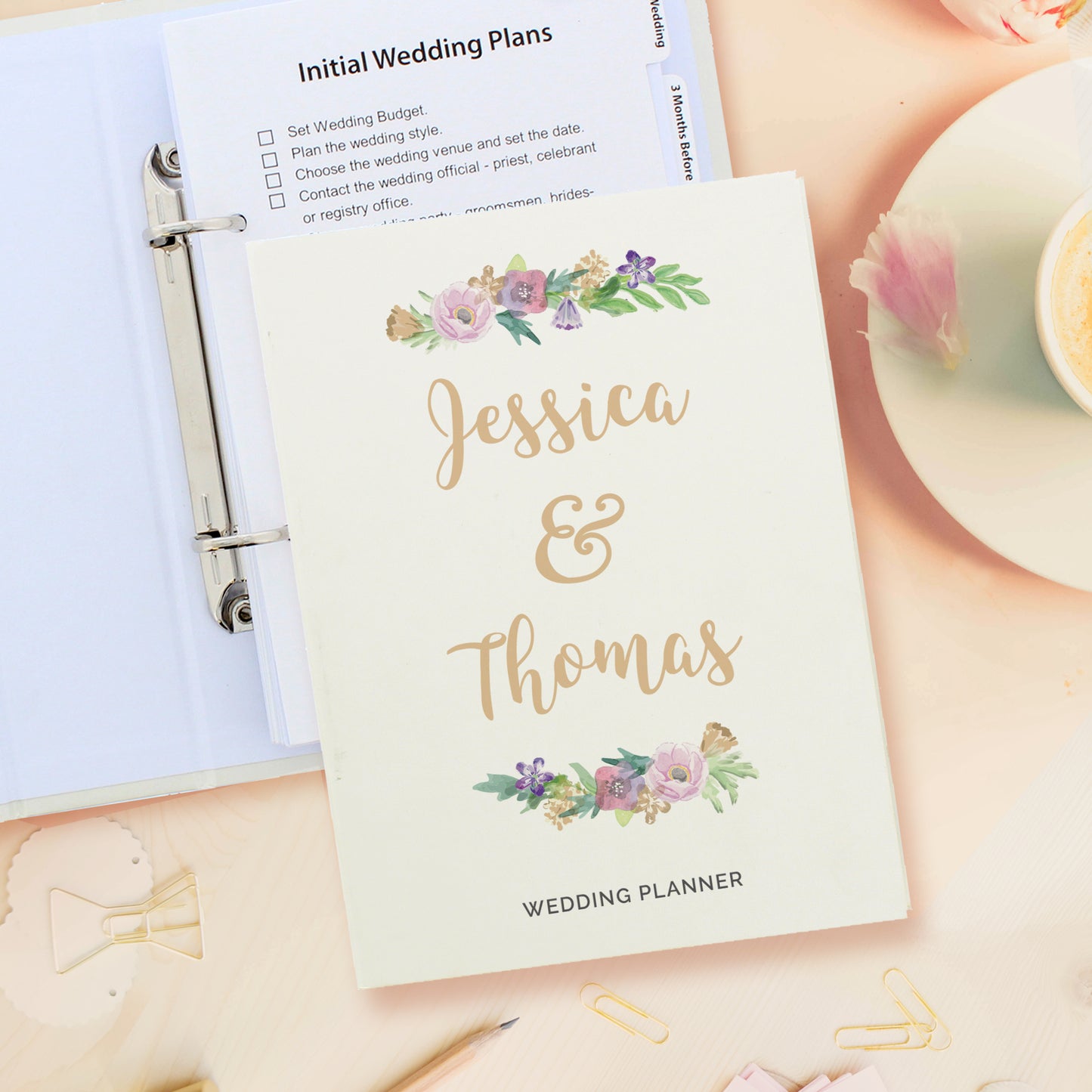 Wedding planner book with floral design and 'Jessica & Thomas' text, placed on a surface with stationery items.