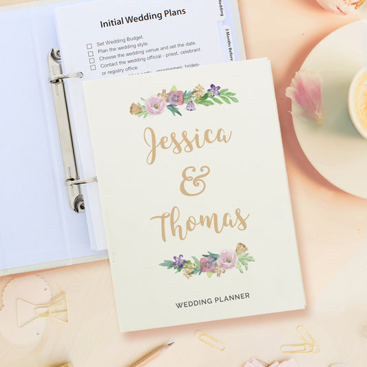 Wedding planner book with floral design and 'Jessica & Thomas' text, placed on a surface with stationery items.