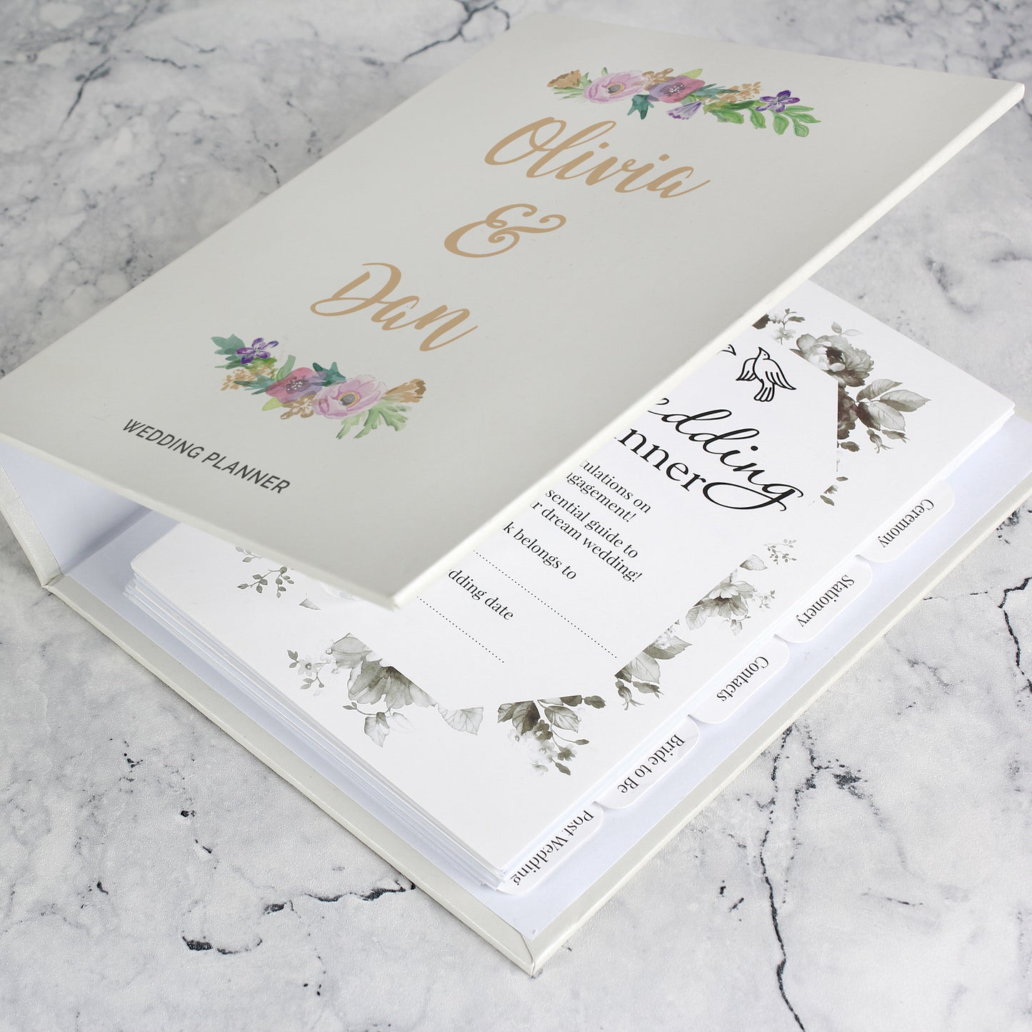 Wedding planner book with floral designs and text on a marble surface