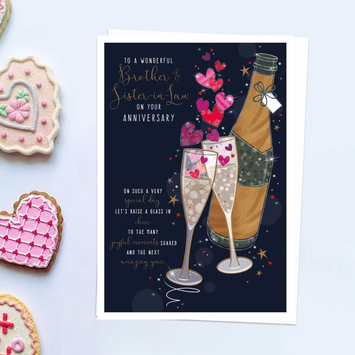 Front image of card with bottle of bubbly and glasses with hearts and verse. Dark background with foil rose gold details