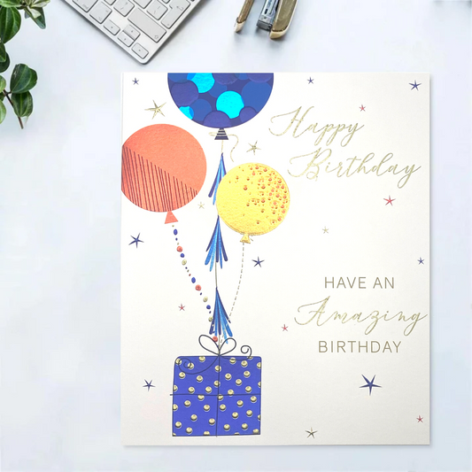White square card with blue orange and gold balloons attached to a gift, with gold text