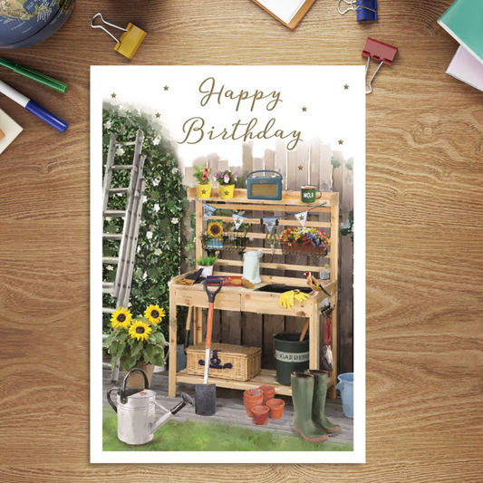 Front image with gardening bench, ladder up hedge and watering can & wellies.