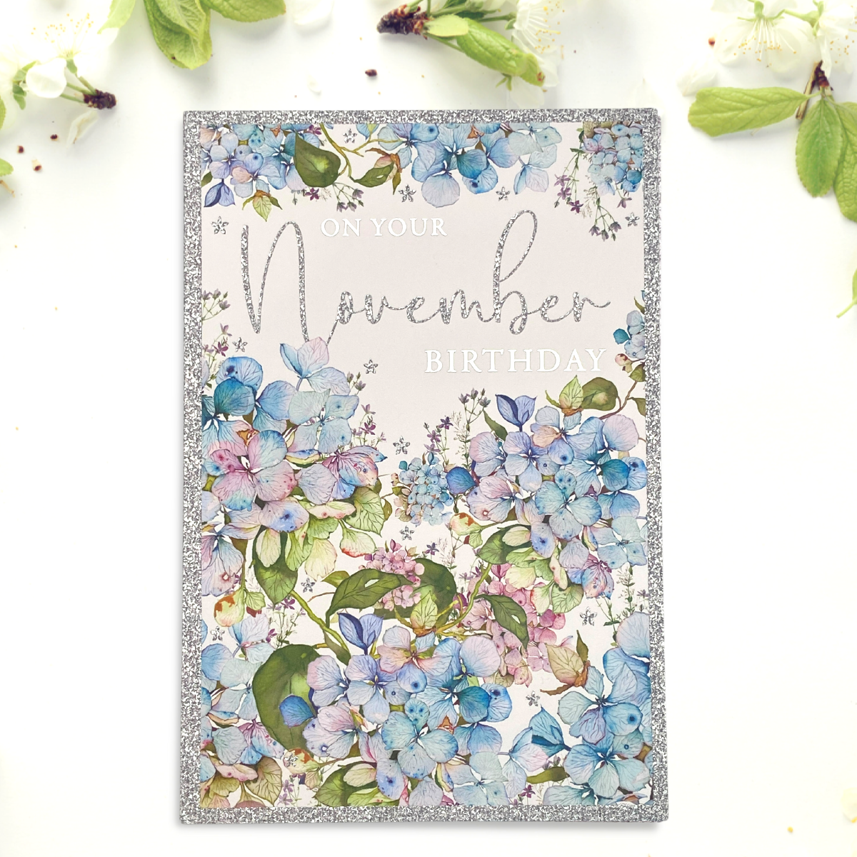 Front image of November birthday card featuring blue hydrangeas and glitter border