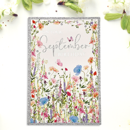 Front image of September birthday card featuring pretty wild flowers and silver glitter border and text