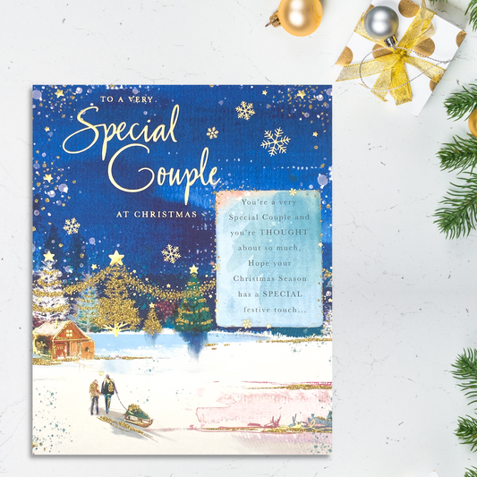 Large blue card with couple pulling sled in the snow walking to decorated house in distance
