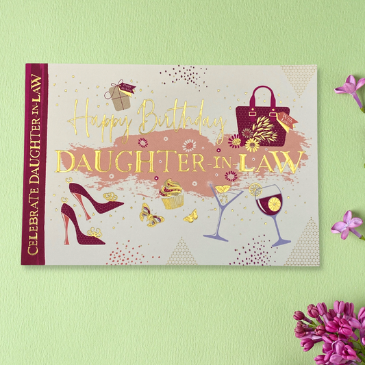 Front image of landscape design card with gold foil text and red colour shoes, handbag, classes and cakes